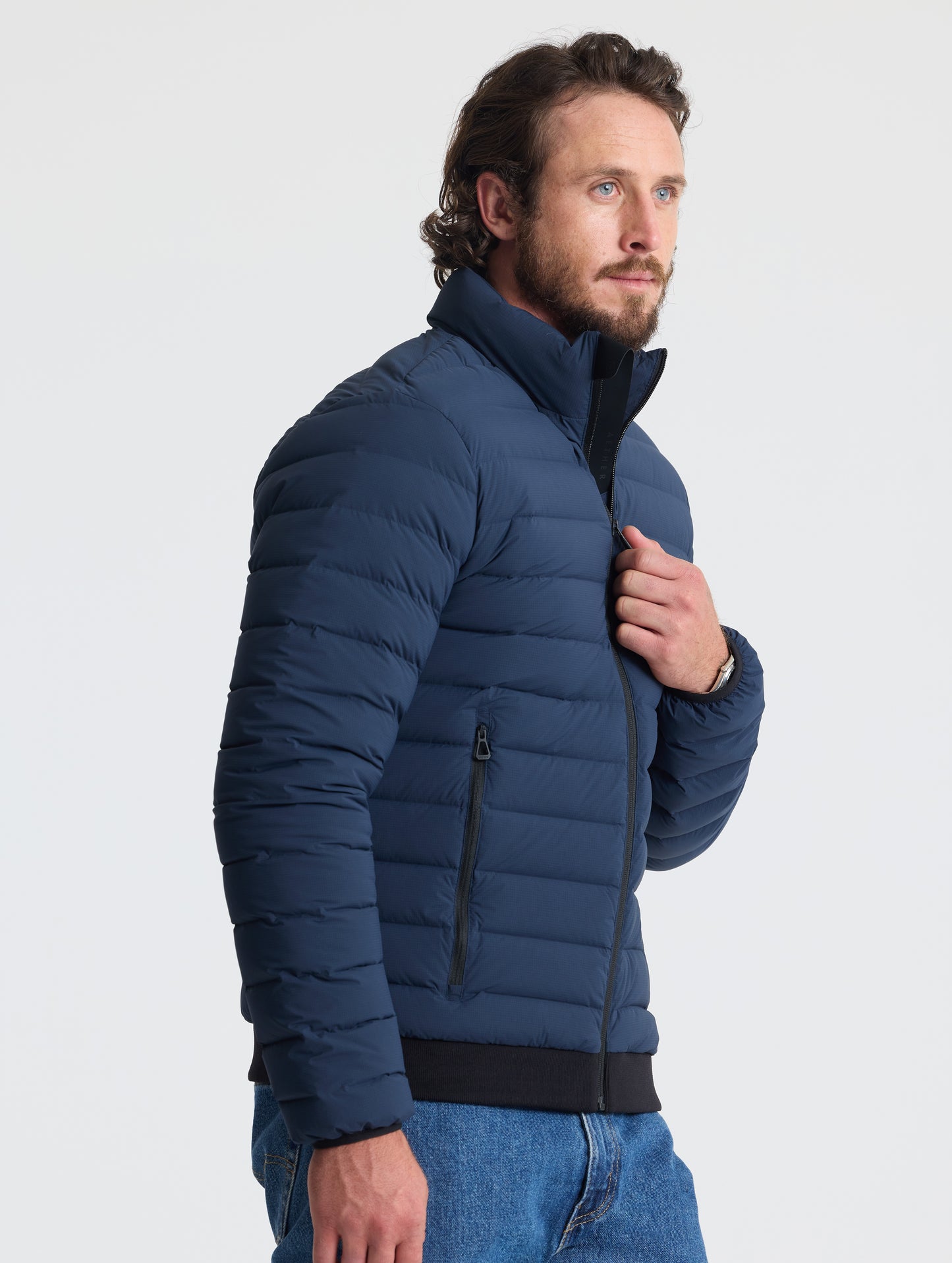 Angled view of man wearing Launch Jacket in Total Eclipse dark blue from AETHER Apparel.