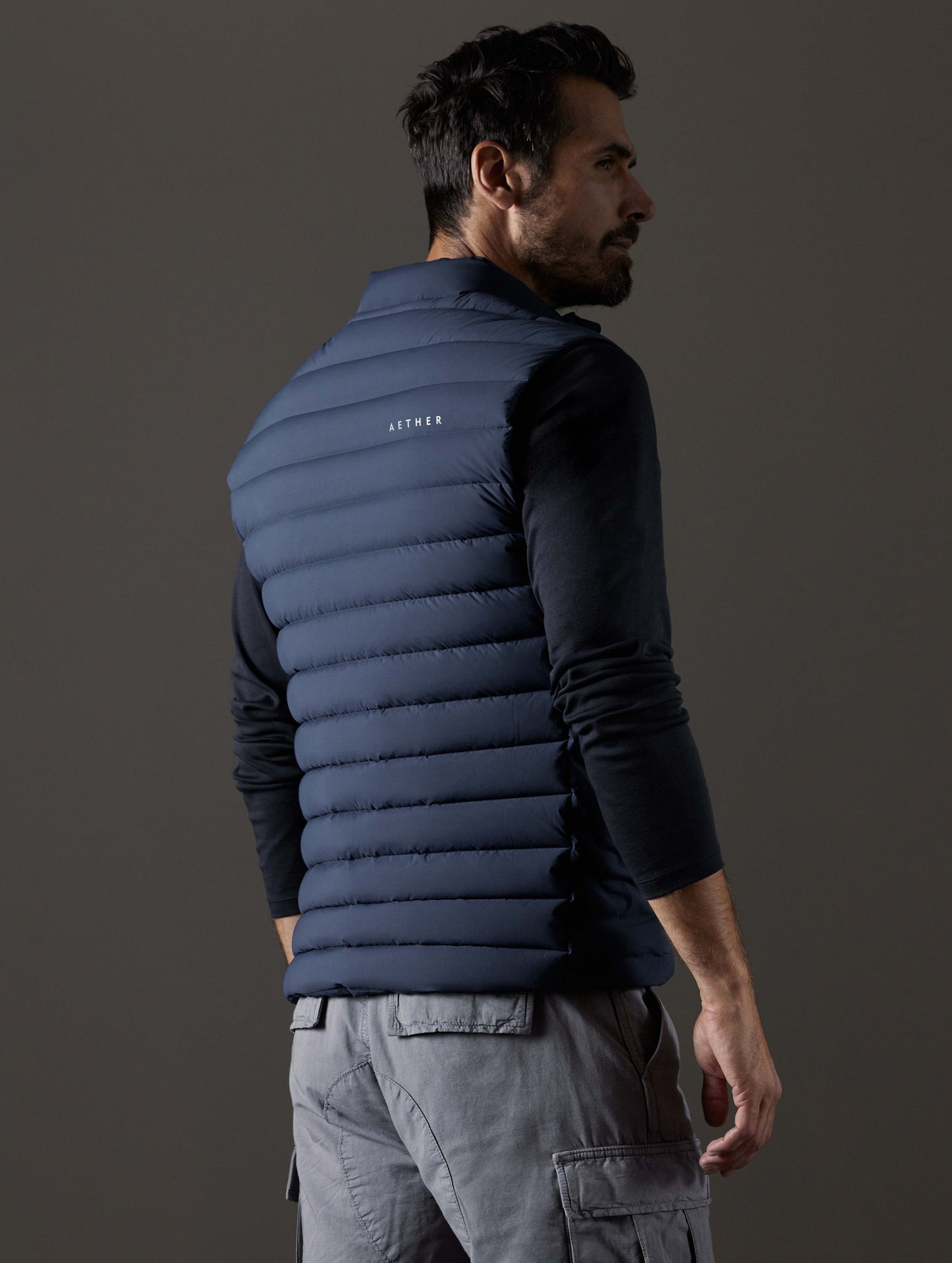 Rear 3/4 body view of man wearing Launch Vest in Total Eclipse dark blue from AETHER Apparel.
