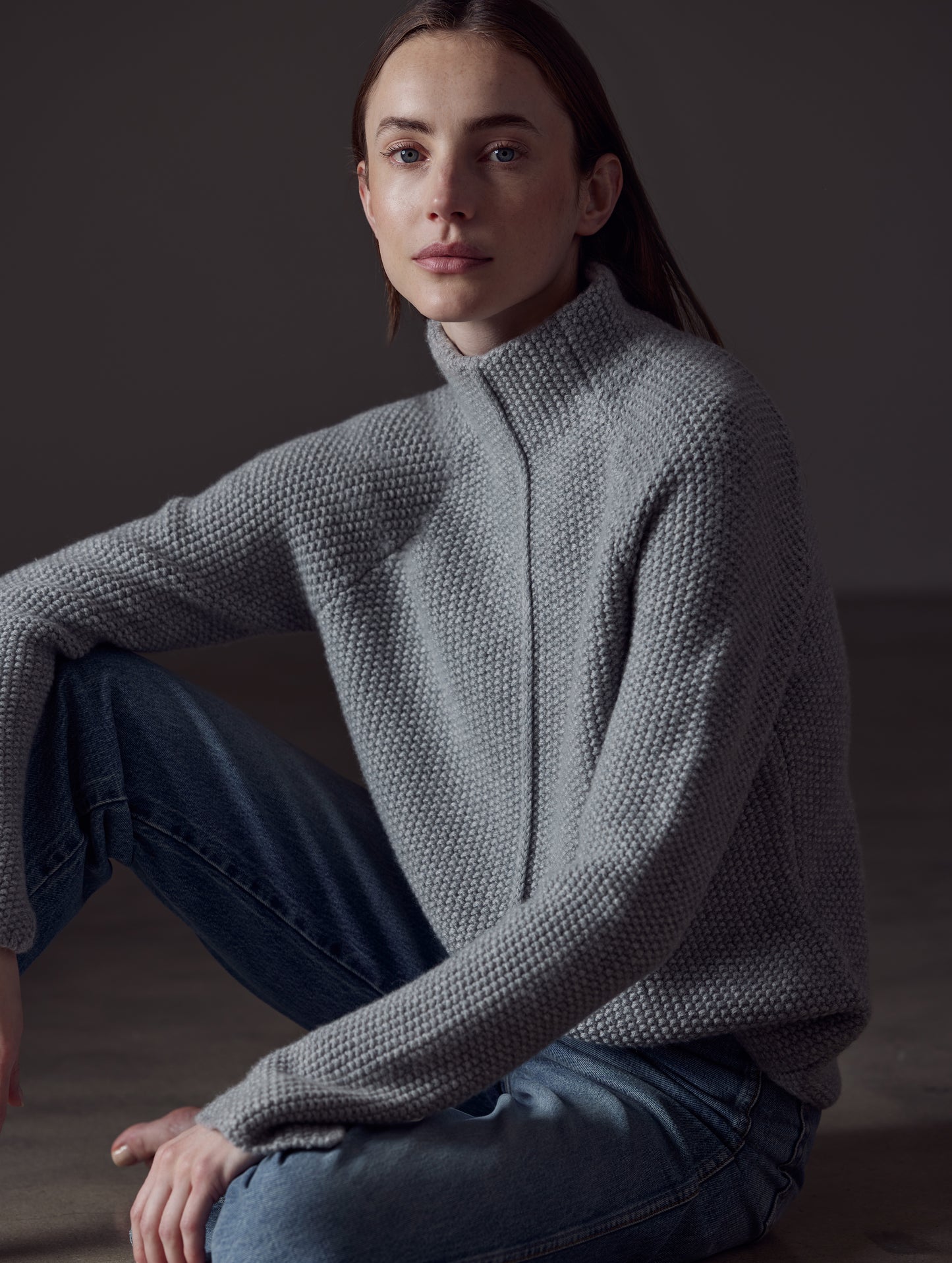 Front angled view of woman sitting on floor wearing Luxe Seamed Sweater in Heather Grey from AETHER Apparel.