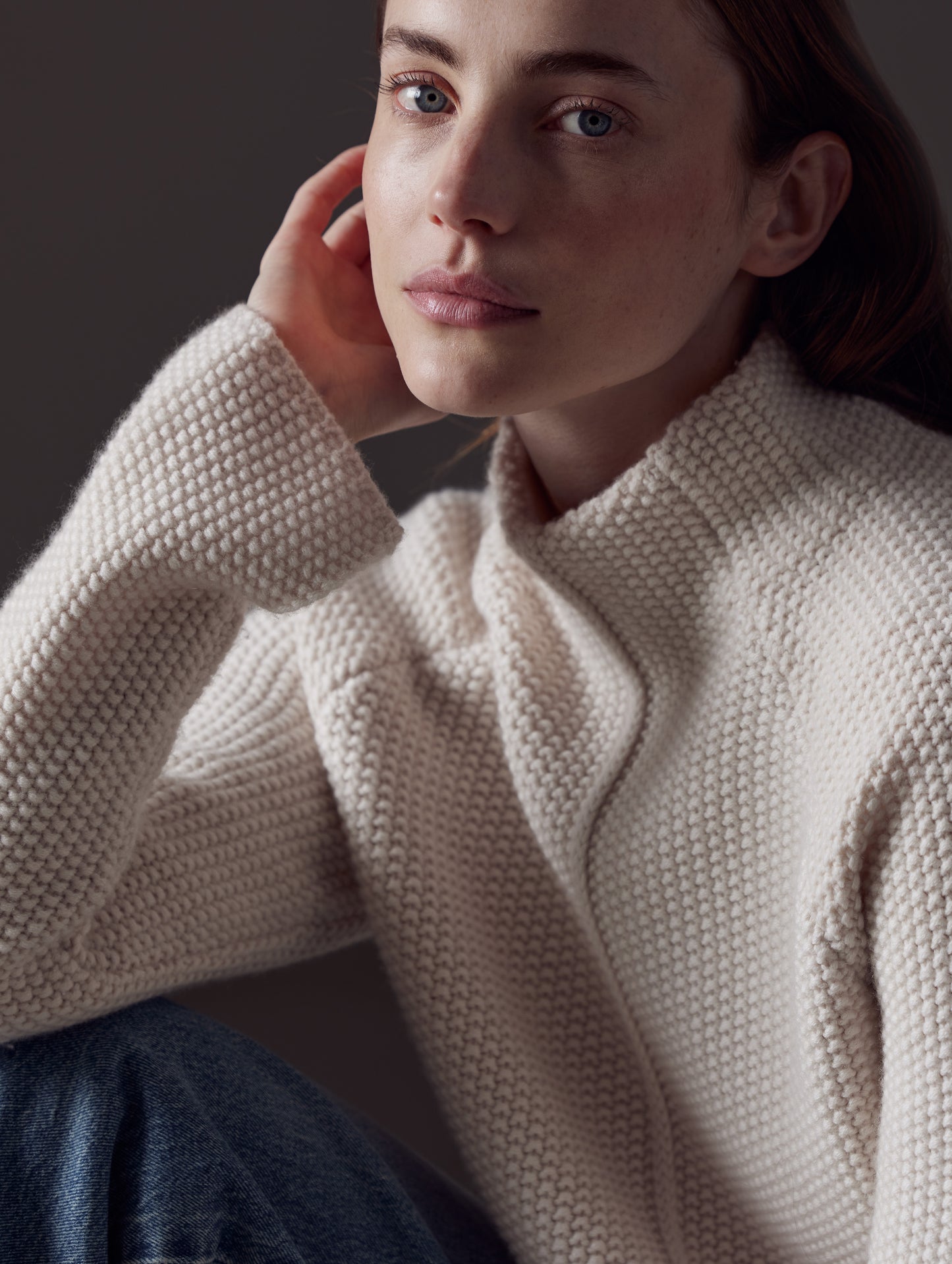 Closeup front angled view of woman sitting down wearing Luxe Seamed Sweater in Winter White from AETHER Apparel.