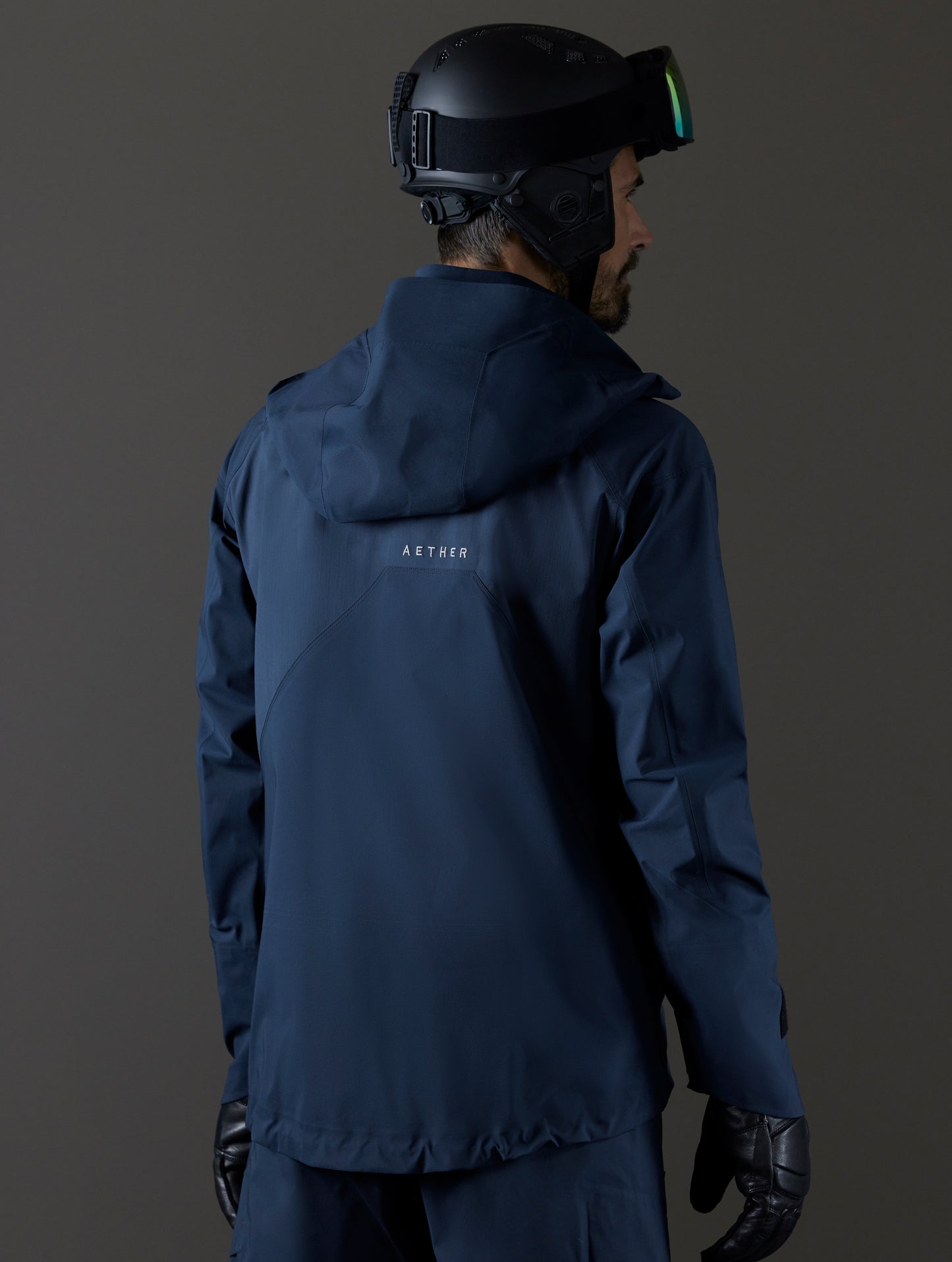 Rear 3/4 body view of man wearing Maverick Snow-Shell Jacket in Total Eclipse dark blue from AETHER Apparel.
