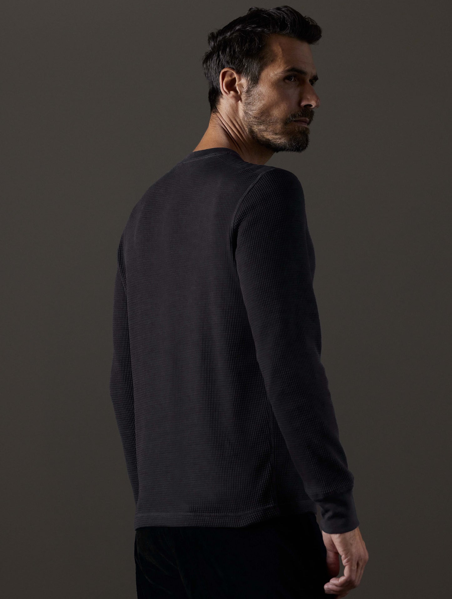 Rear 3/4 body view of man wearing Milford Waffle Henley in Onyx Black from AETHER Apparel.