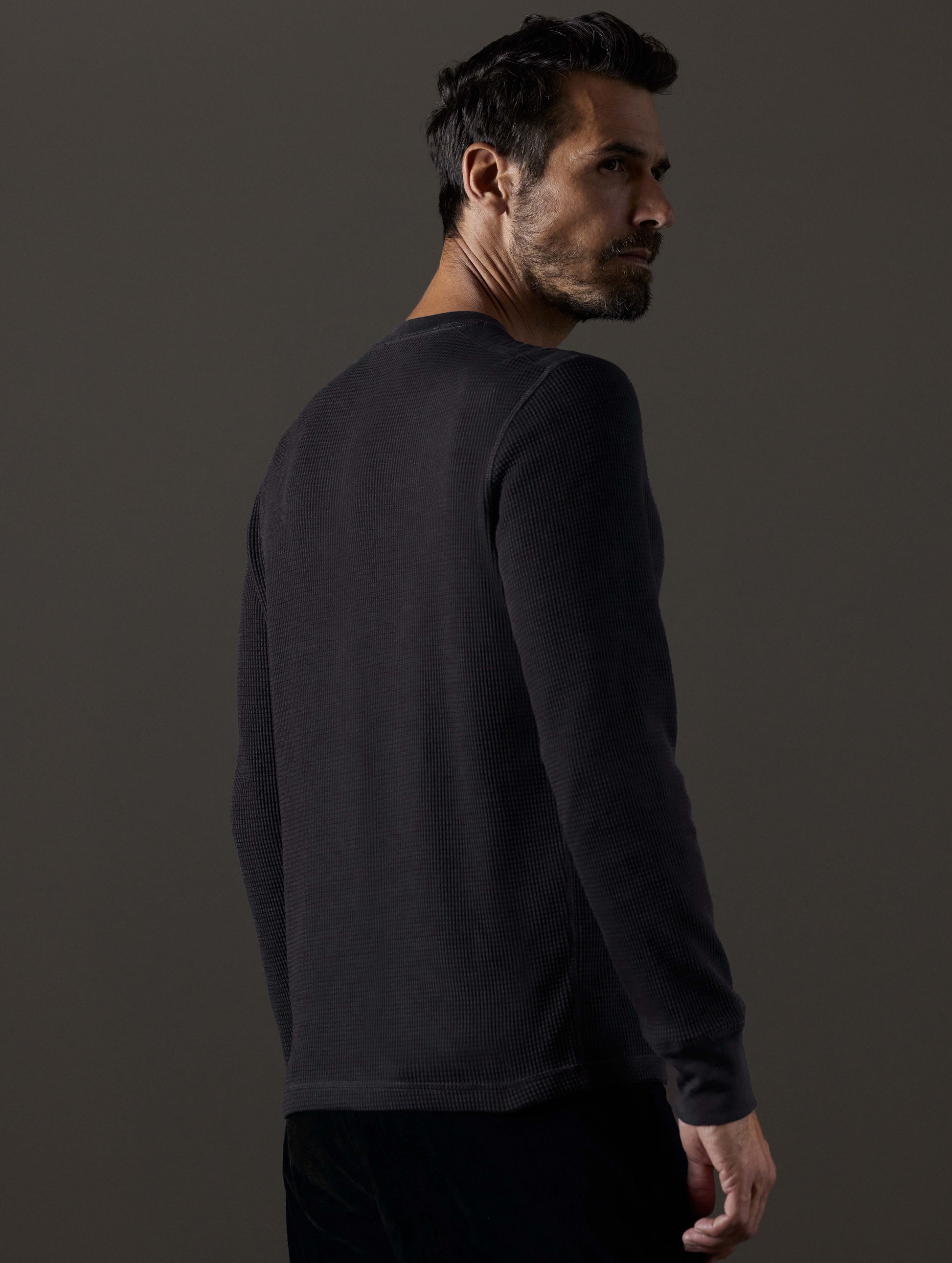 Rear 3/4 body view of man wearing Milford Waffle Henley in Onyx Black from AETHER Apparel.