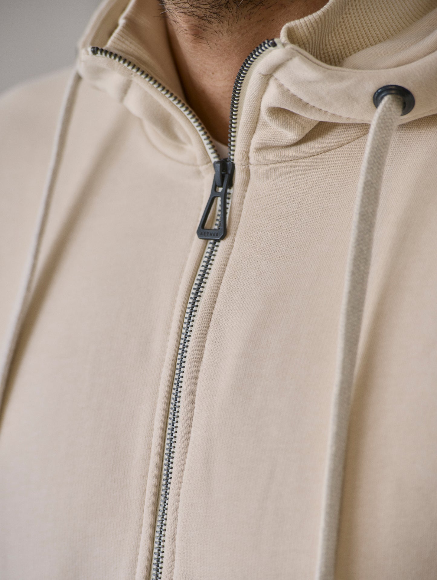 Closeup image of main center-front zipper with custom-branded zipper pull on Monte Full-Zip Hoodie in Bone white from AETHER Apparel.