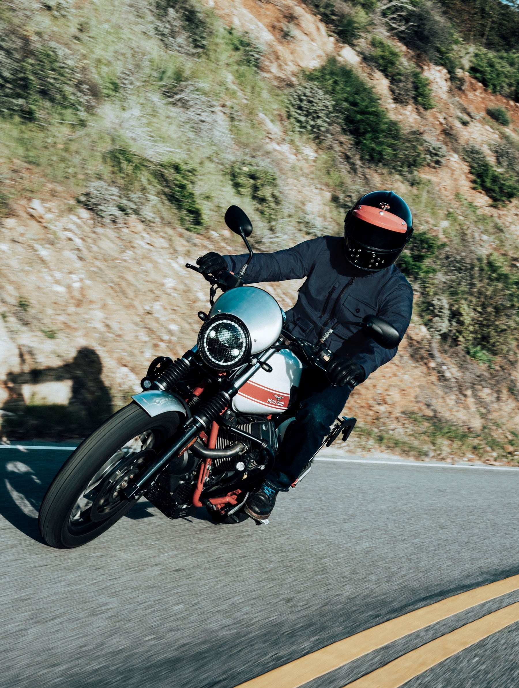 Outdoor lifestyle view of man riding a Moto Guzzi motorcycle wearing the Mulholland Motorcycle Jacket in Total Eclipse dark blue from AETHER Apparel.