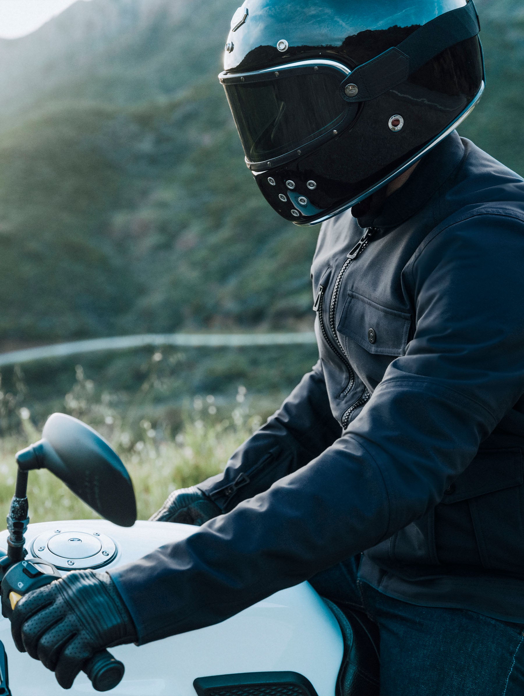 Outdoor lifestyle, profile view of man sitting on a motorcycle wearing the Mulholland Motorcycle Jacket in Total Eclipse dark blue from AETHER Apparel.
