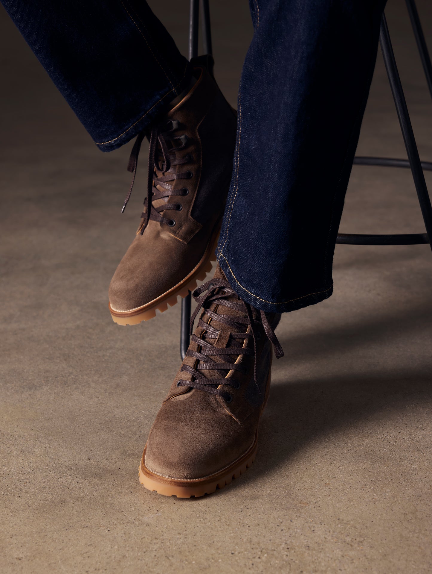 Closeup lifestyle image of feet of man sitting on stool wearing Ojai City Boot in Bison Brown suede and canvas from AETHER Apparel.