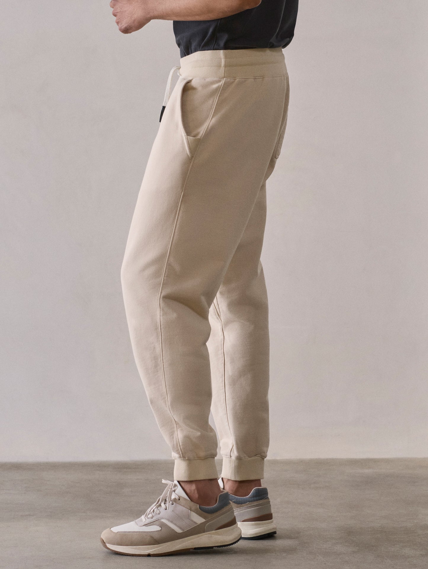 Left side lower body profile view of man wearing Osa Cuffed Sweatpant in Bone white from AETHER Apparel.