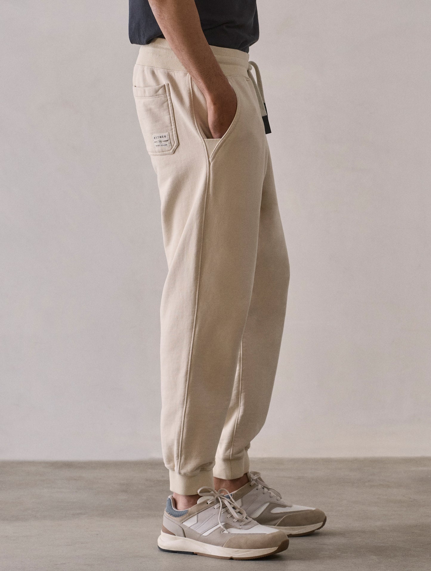 Right side lower body profile view of man wearing Osa Cuffed Sweatpant in Bone white from AETHER Apparel.