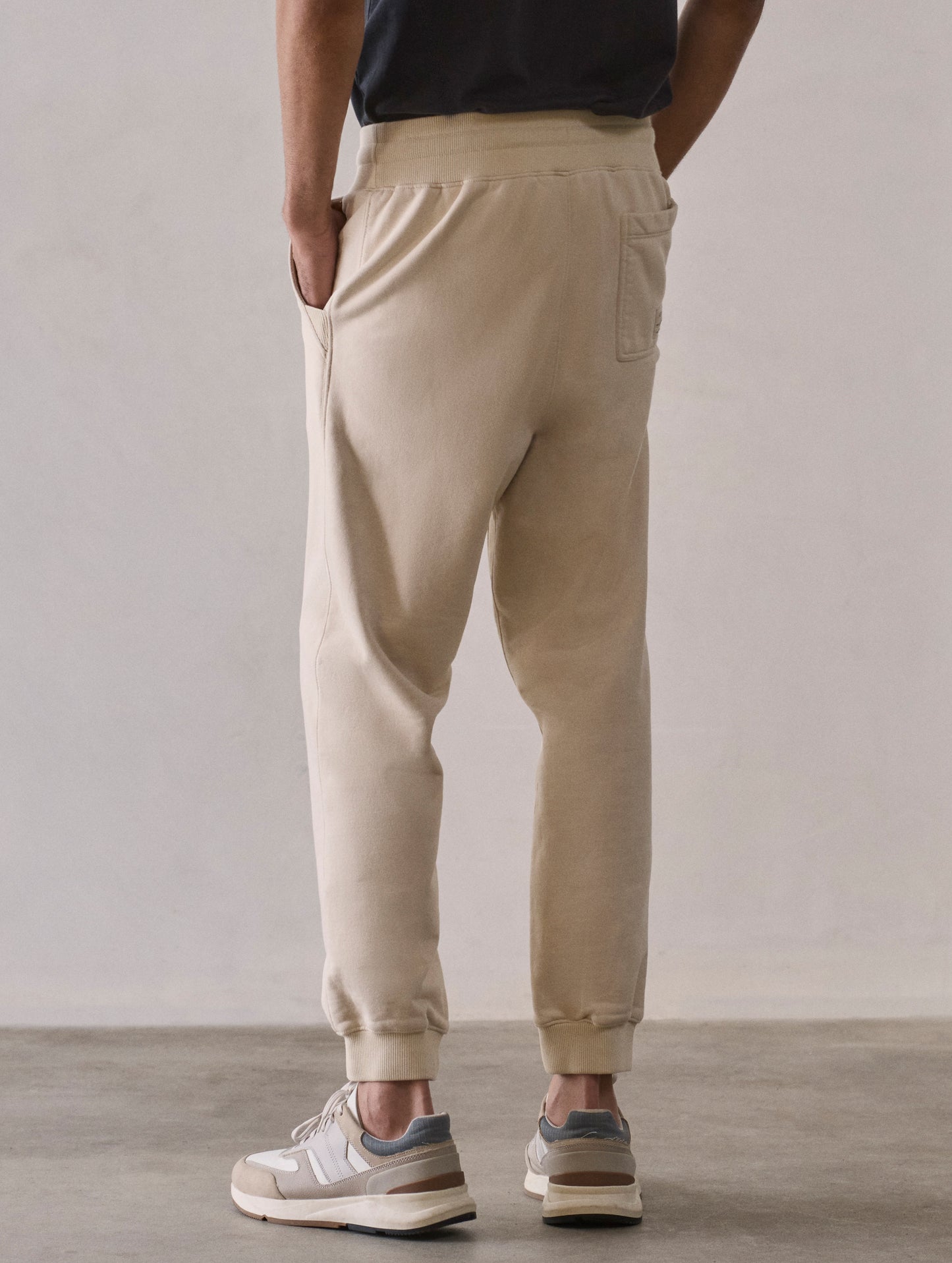 Rear 3/4 lower body view of man wearing Osa Cuffed Sweatpant in Bone white from AETHER Apparel.