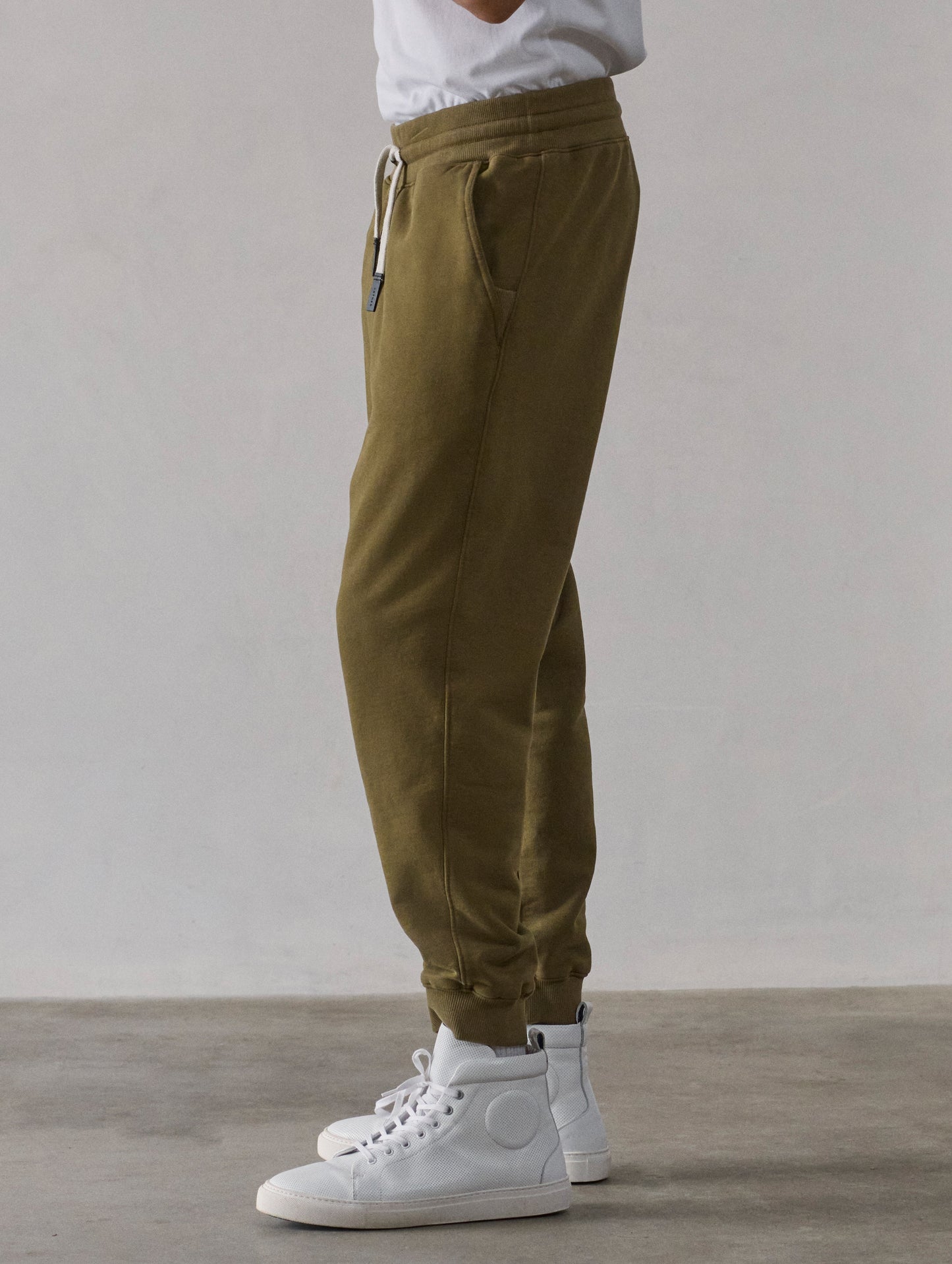 Left side profile lower-body view of man wearing Osa Cuffed Sweatpant in Command Green from AETHER Apparel.