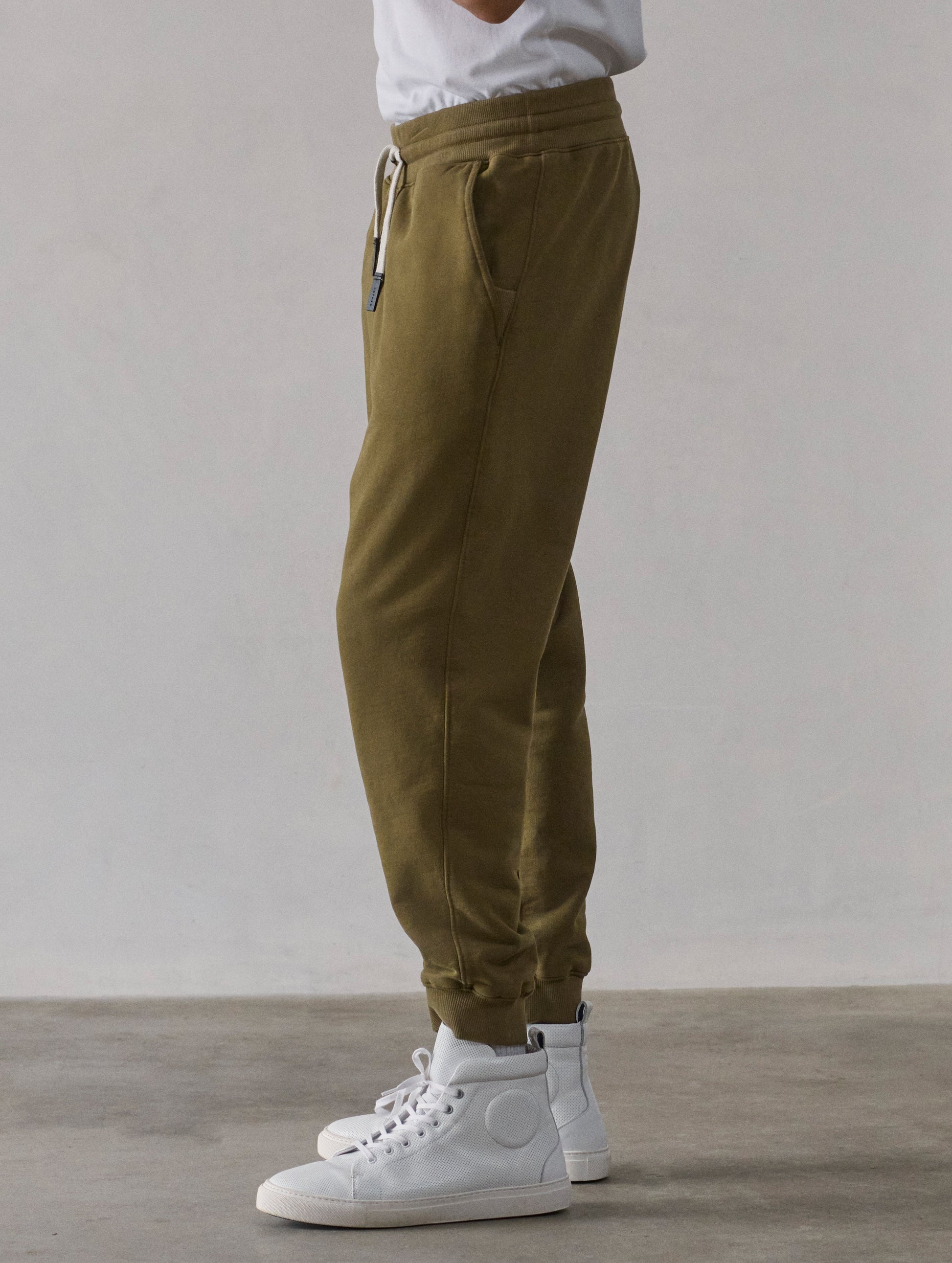 Left side profile lower-body view of man wearing Osa Cuffed Sweatpant in Command Green from AETHER Apparel.