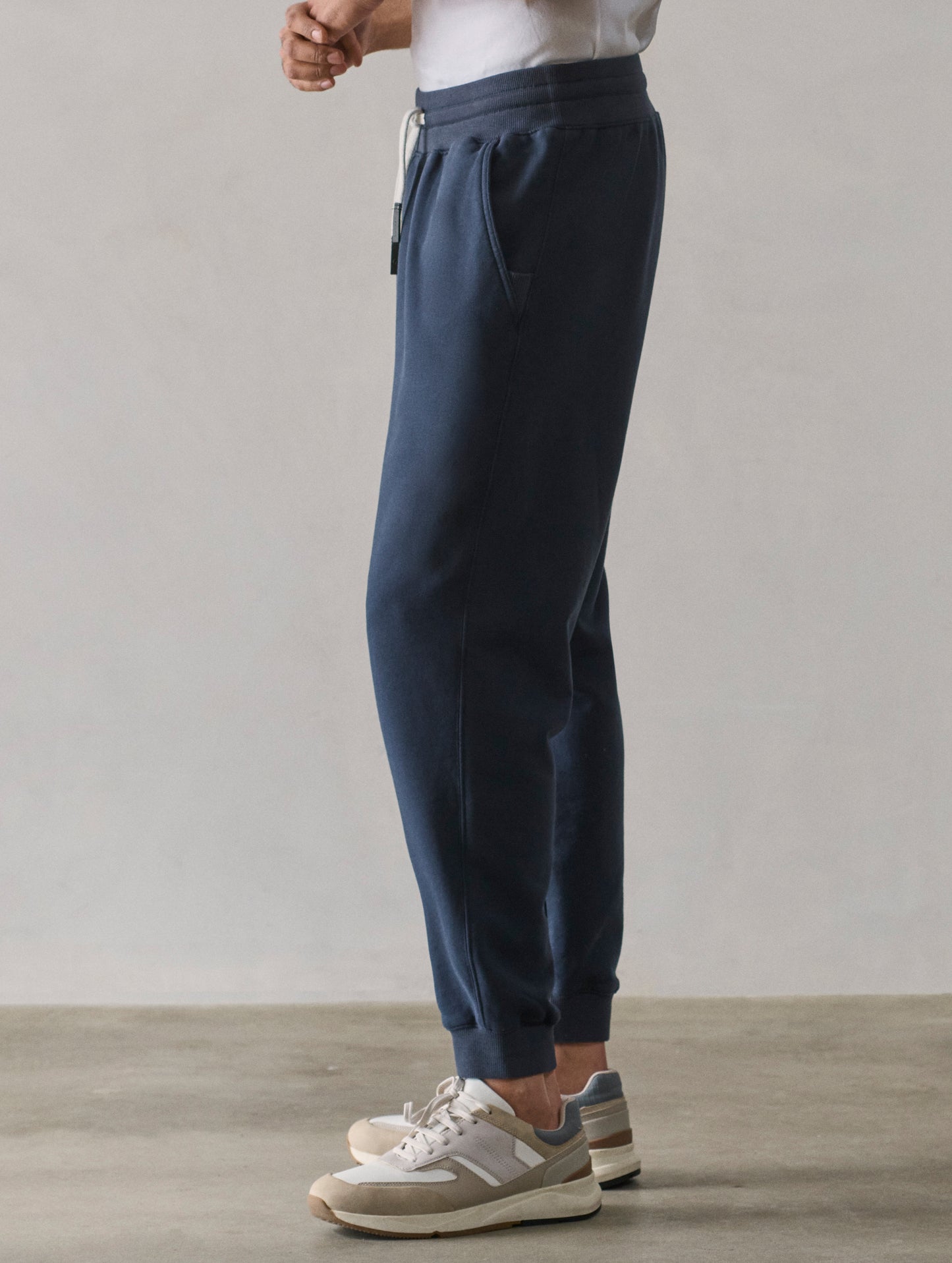 Left side lower body profile view of man wearing Osa Cuffed Sweatpant in Total Eclipse dark blue from AETHER Apparel.