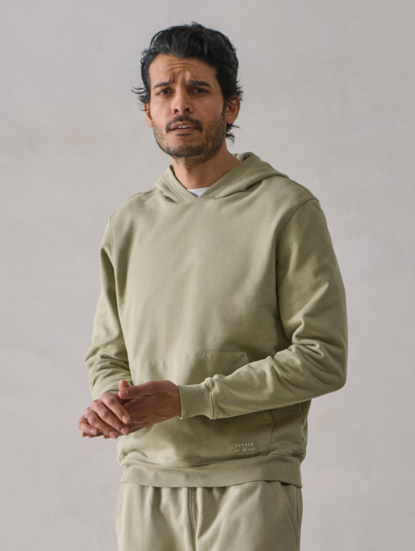 Front upper body view of man wearing Osa Pullover Hoodie in Sage Green from AETHER Apparel.