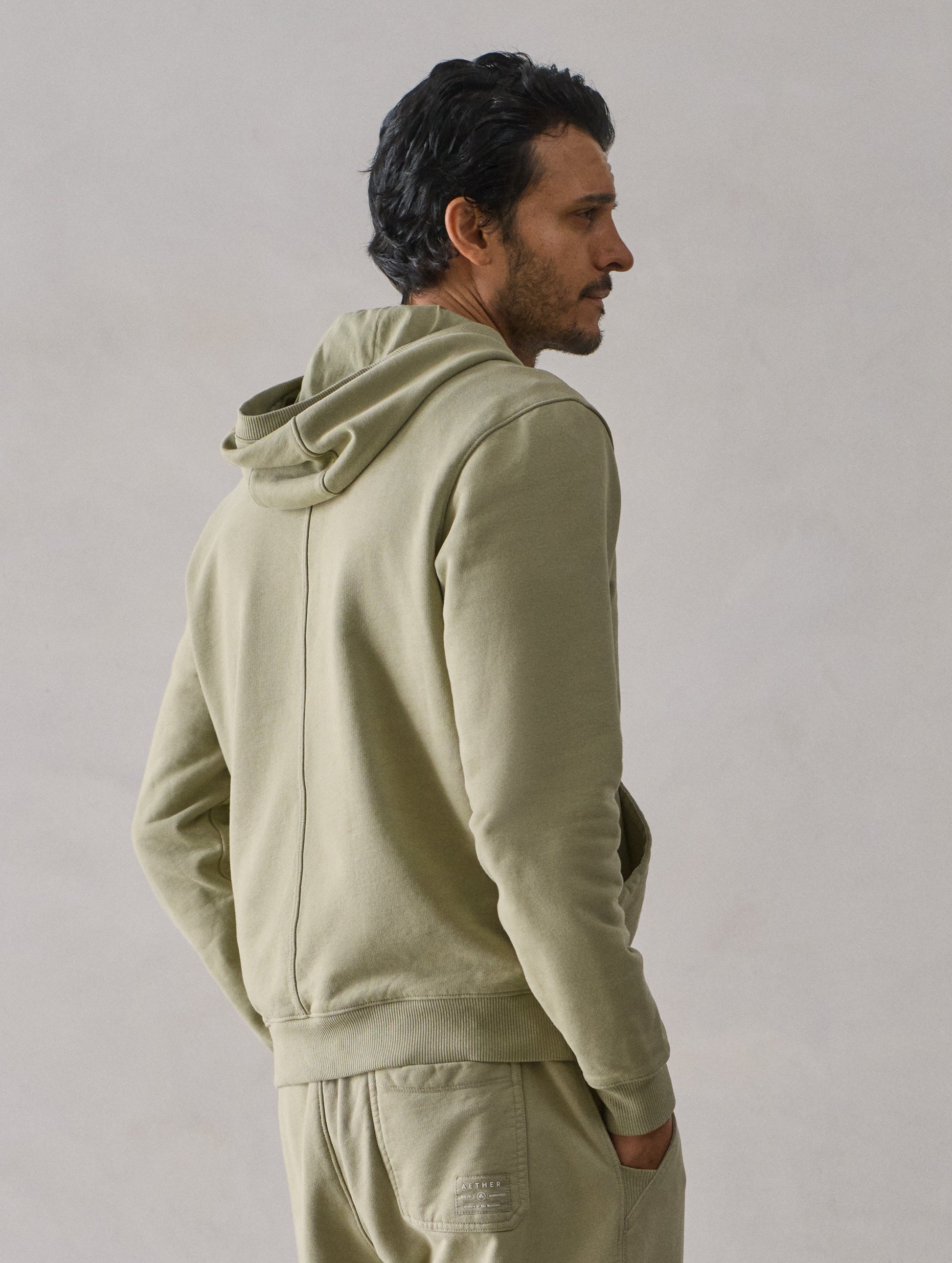 Rear 3/4 upper body view of man wearing Osa Pullover Hoodie in Sage Green from AETHER Apparel.