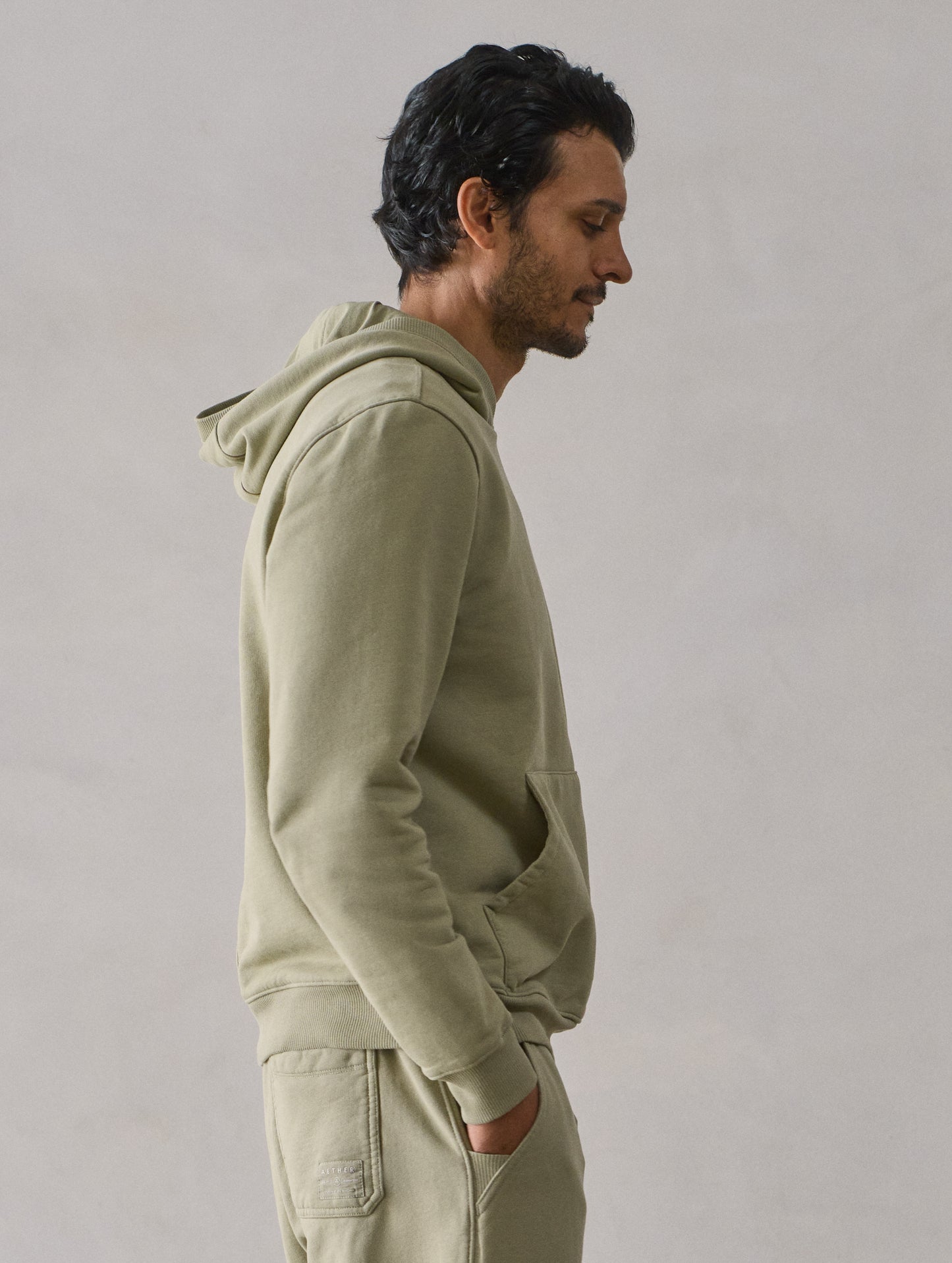 Right side upper body profile view of man wearing Osa Pullover Hoodie in Sage Green from AETHER Apparel.