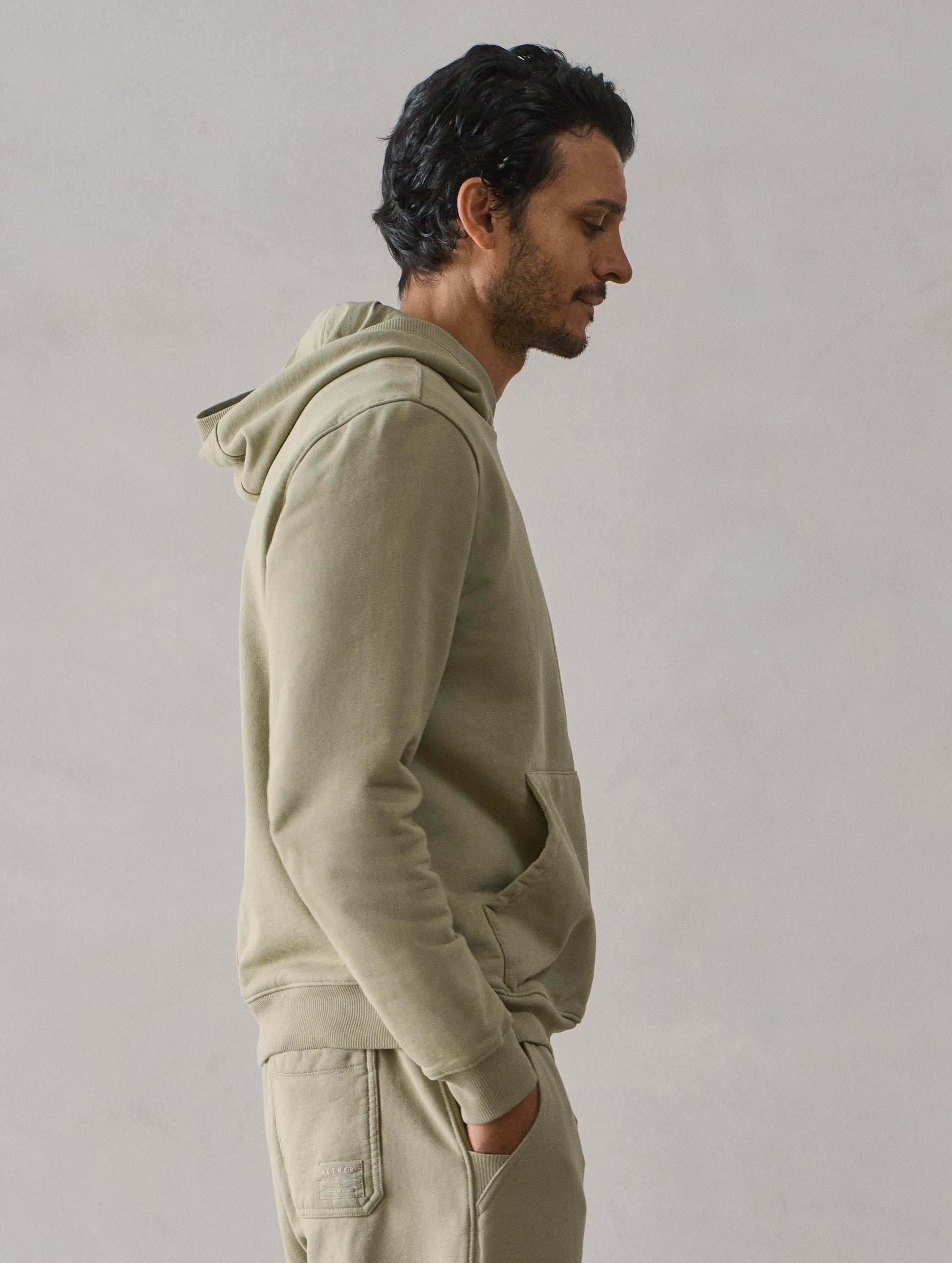 Right side upper body profile view of man wearing Osa Pullover Hoodie in Sage Green from AETHER Apparel.