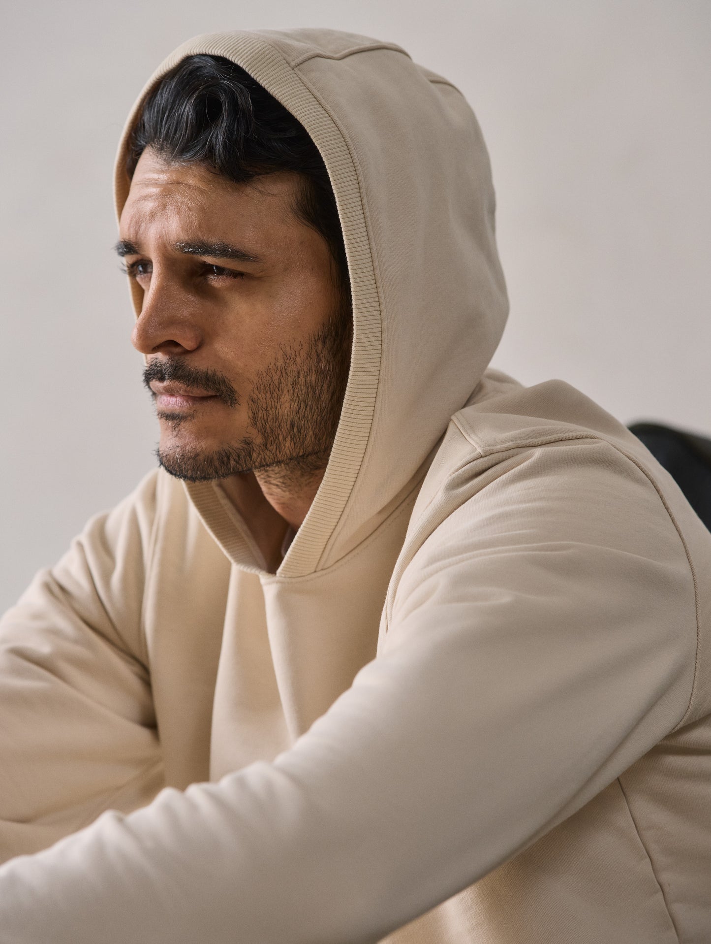 Front 3/4 upper body closeup view of man with hood up wearing Osa Pullover Hoodie in Bone white from AETHER Apparel.