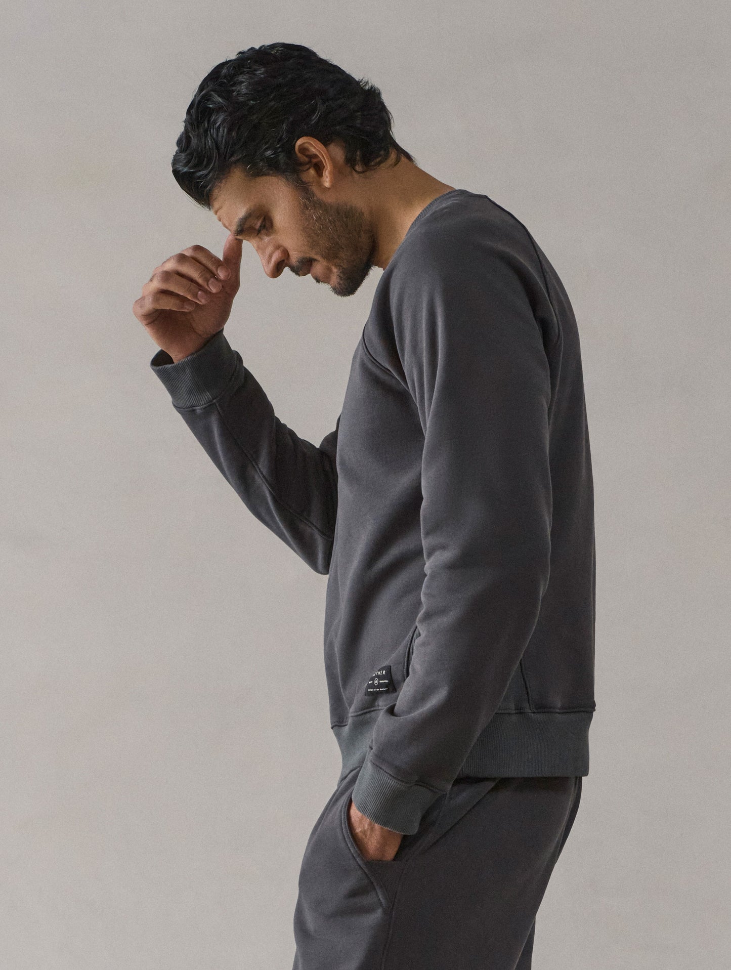 Left side profile upper-body view of man wearing Osa Raglan Sweatshirt in Graphite grey from AETHER Apparel.