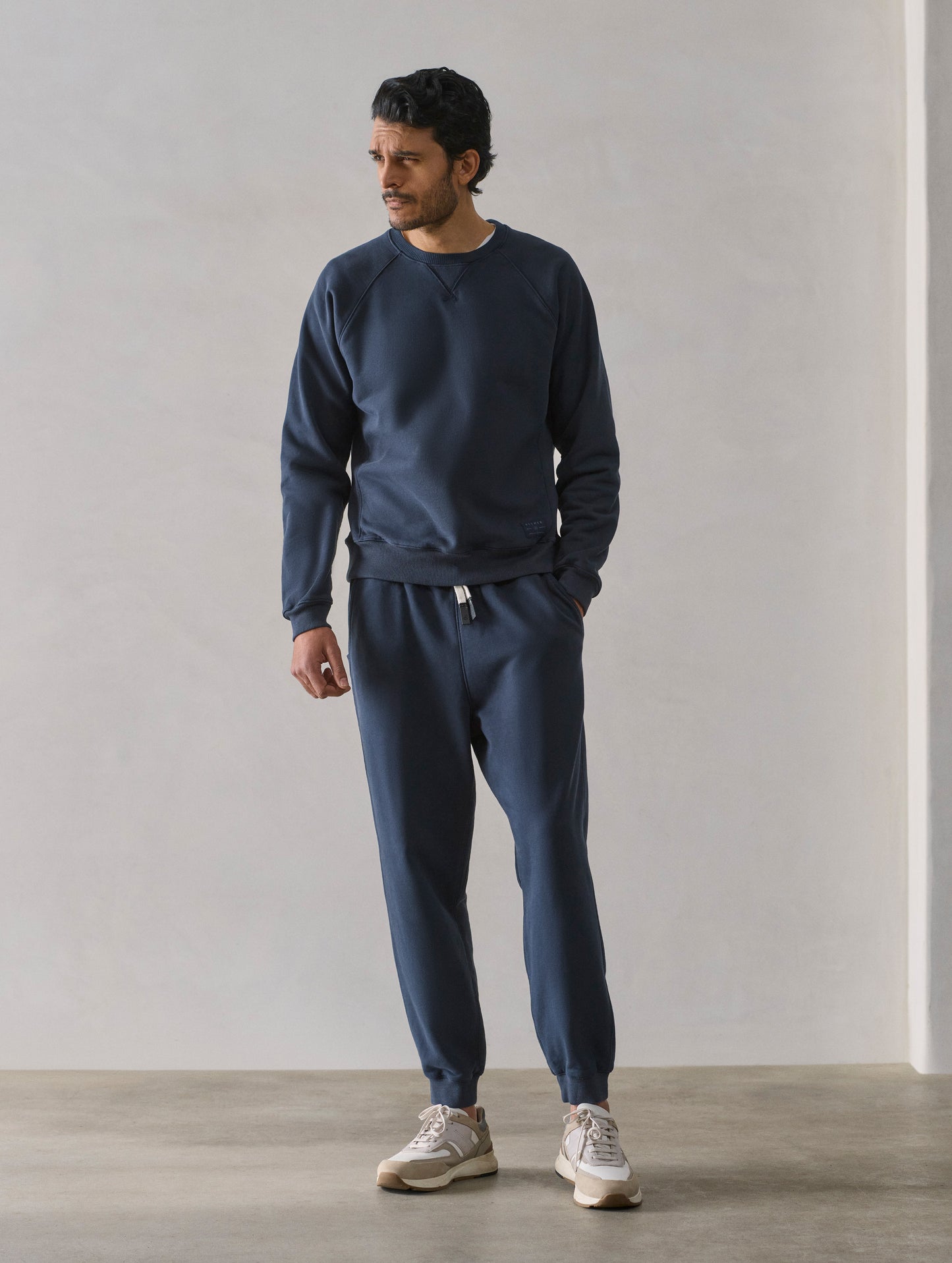 Front full-body view of man wearing Osa Raglan Sweatshirt in Total Eclipse dark blue from AETHER Apparel.