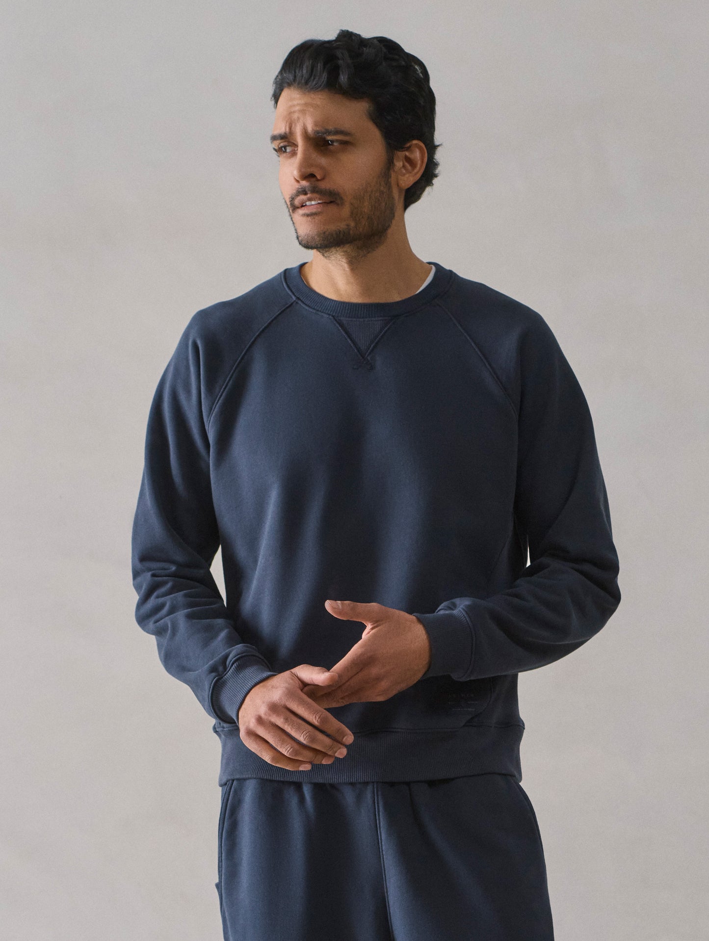 Front upper body view of man wearing Osa Raglan Sweatshirt in Total Eclipse dark blue from AETHER Apparel.