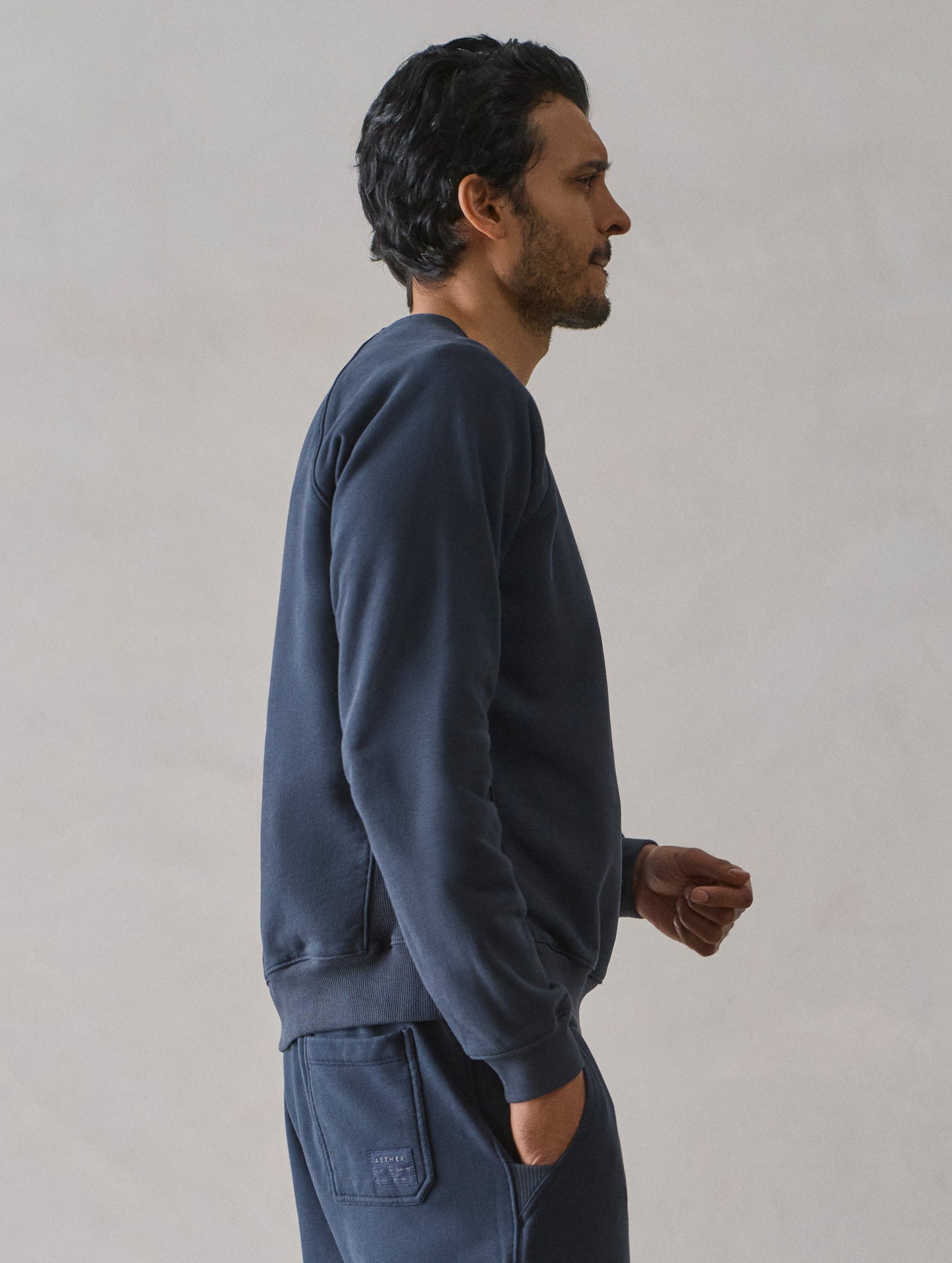 Right side upper body profile view of man wearing Osa Raglan Sweatshirt in Total Eclipse dark blue from AETHER Apparel.