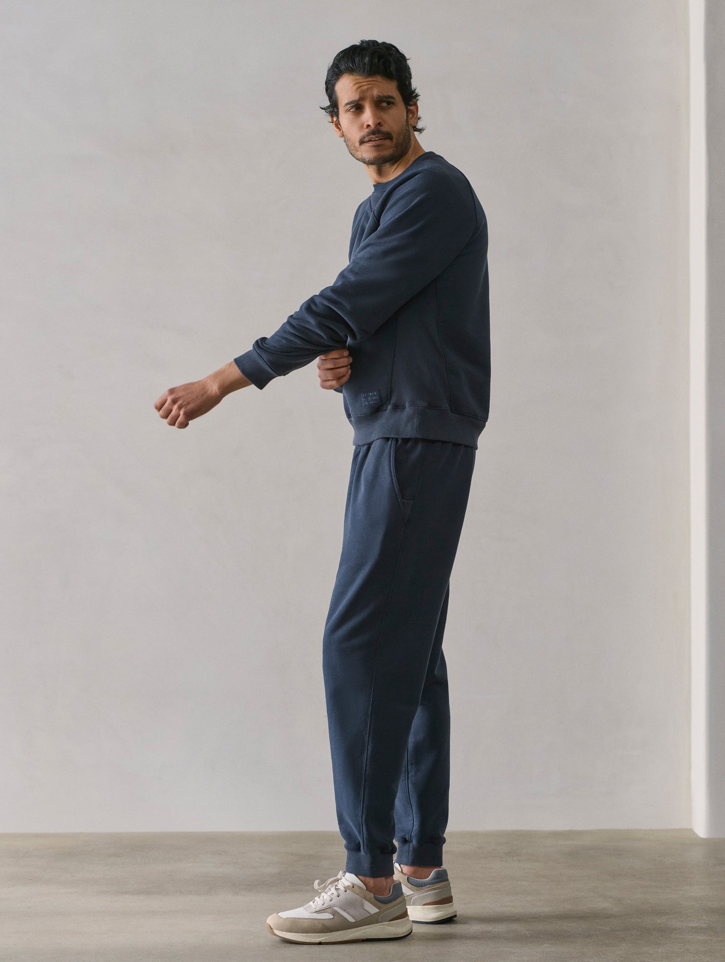 Side profile full-body view of man wearing Osa Raglan Sweatshirt in Total Eclipse dark blue from AETHER Apparel.