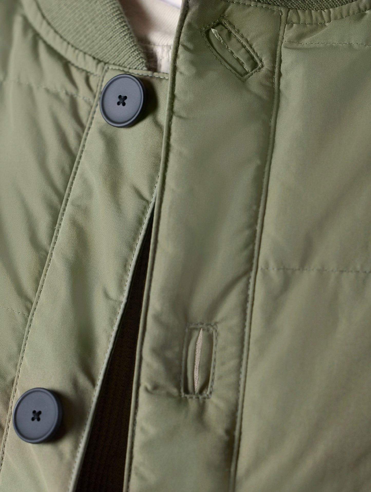 Closeup detailed view of the button-secured main center-front closure on the Pacer Jacket in Fern Green from AETHER Apparel.