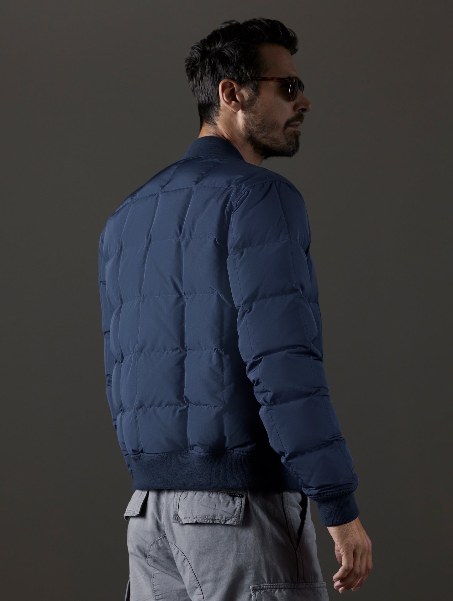 Rear 3/4 body view of man wearing Pacer Jacket in Total Eclipse blue from AETHER Apparel.