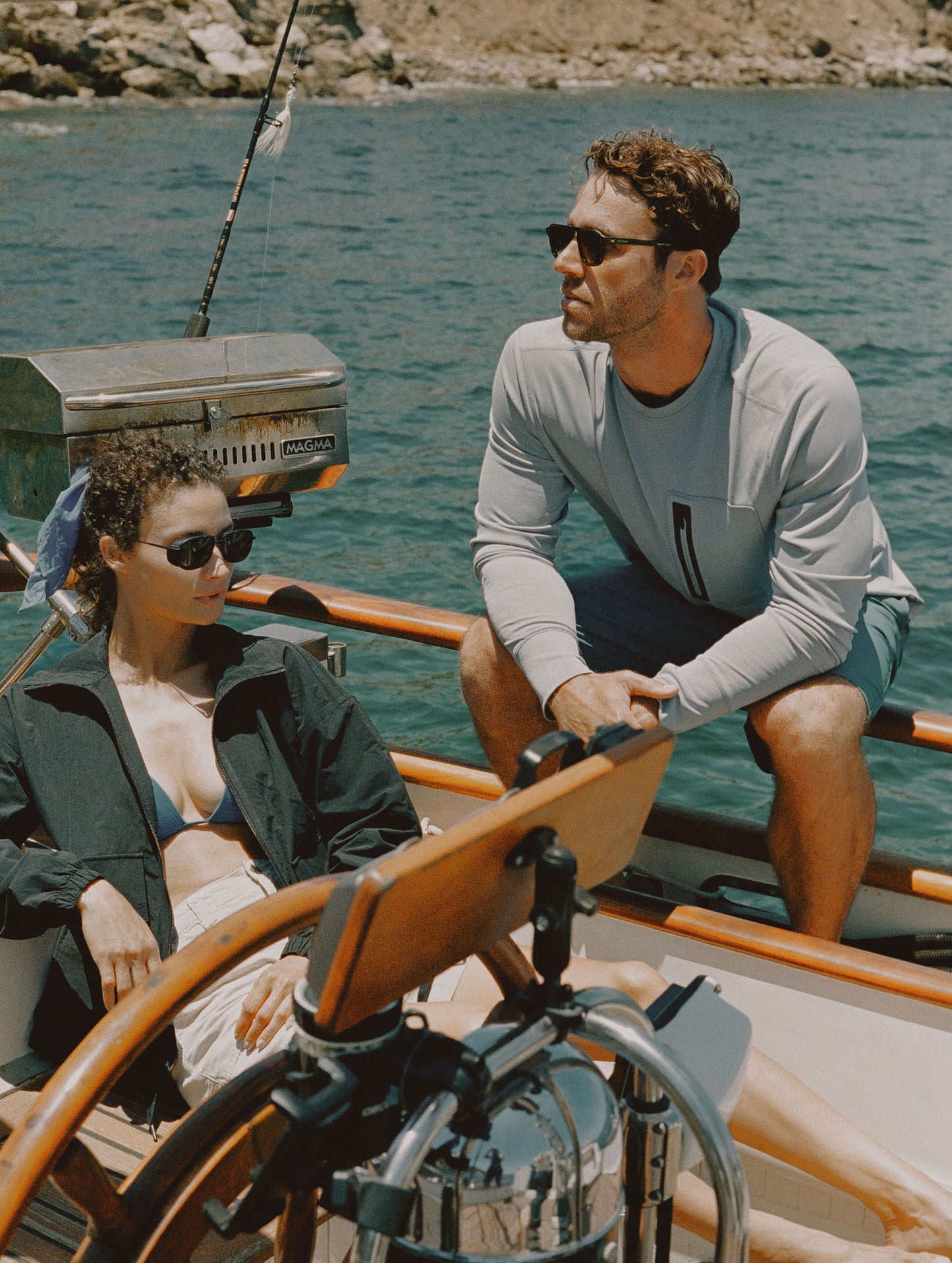 Lifestyle image of man sitting on railing of a boat wearing the Pacific Crewneck Sun Shirt in Sky Grey from AETHER Apparel.