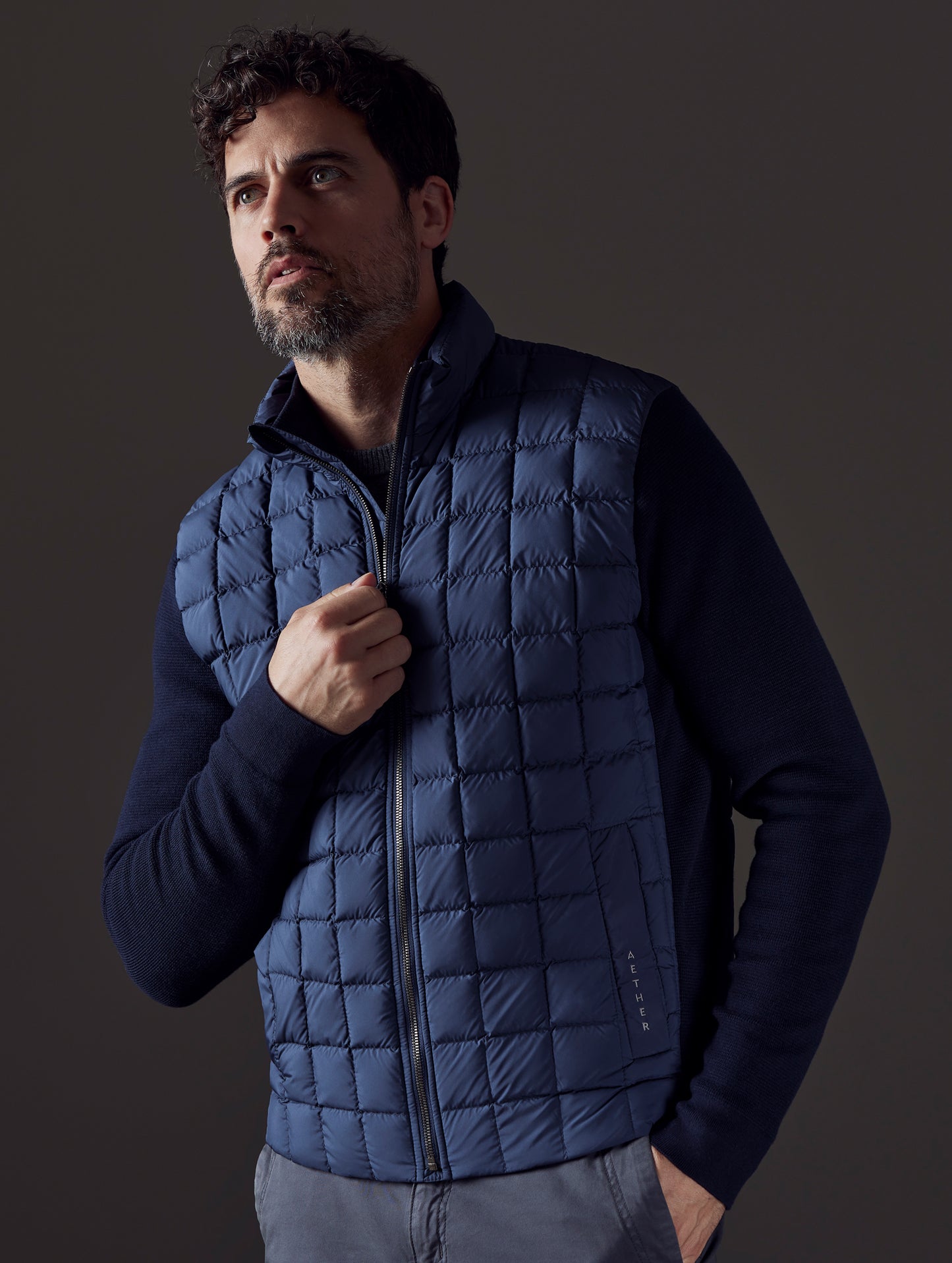 Front 3/4 body view of man with hand on zipper of Phase Full-Zip in Total Eclipse dark blue from AETHER Apparel.
