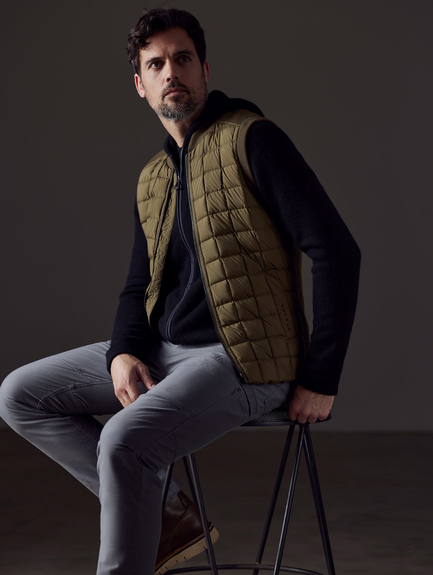 Front 3/4 body view of man sitting wearing Phase Vest in Command Green from AETHER Apparel.