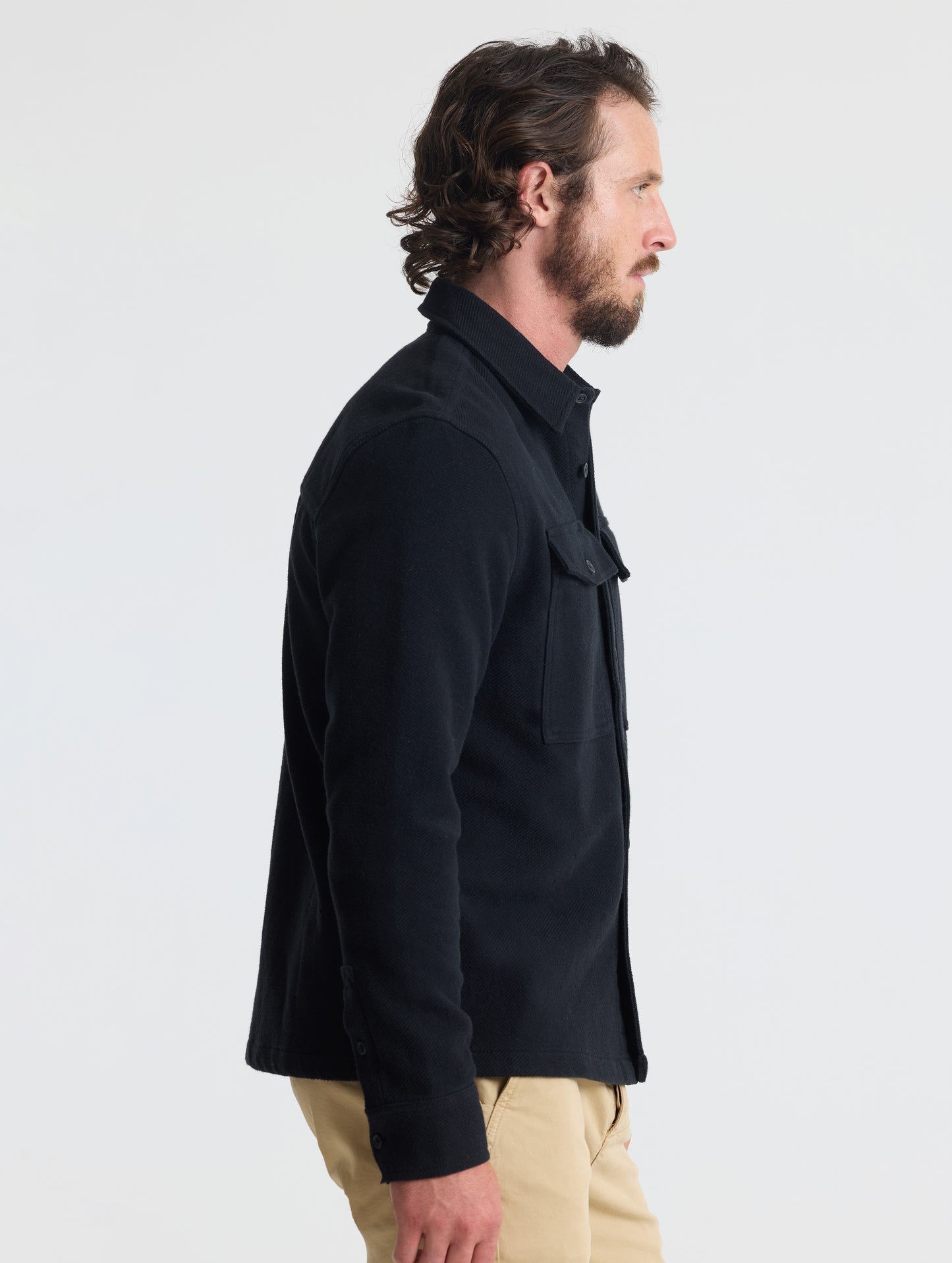 Side profile upper-body view of man wearing Pioneer Heavyweight Button-Down in Onyx Black from AETHER Apparel.
