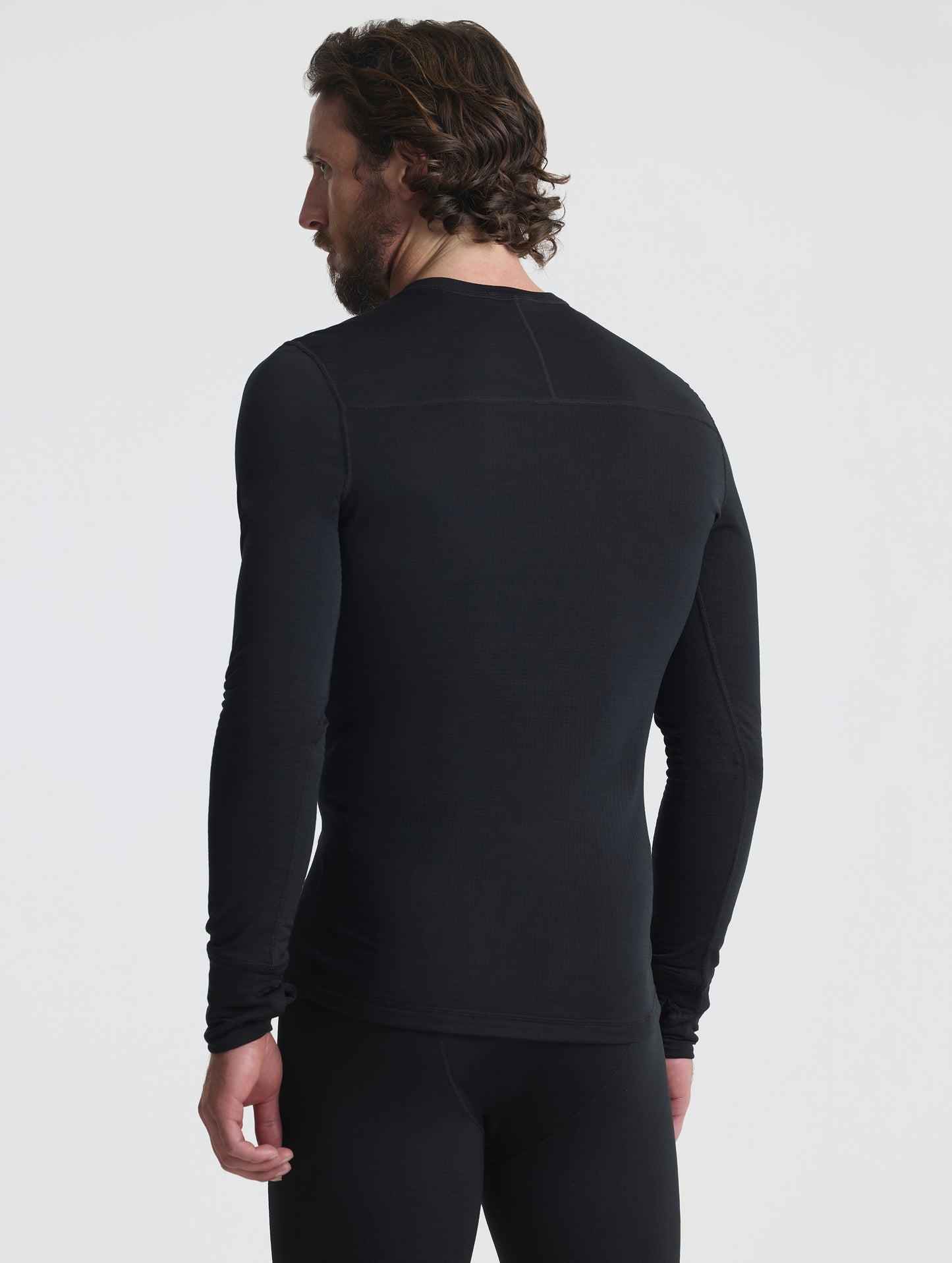 Rear angled upper-body view of man wearing Polar Base Layer Crew in Onyx Black from AETHER Apparel.