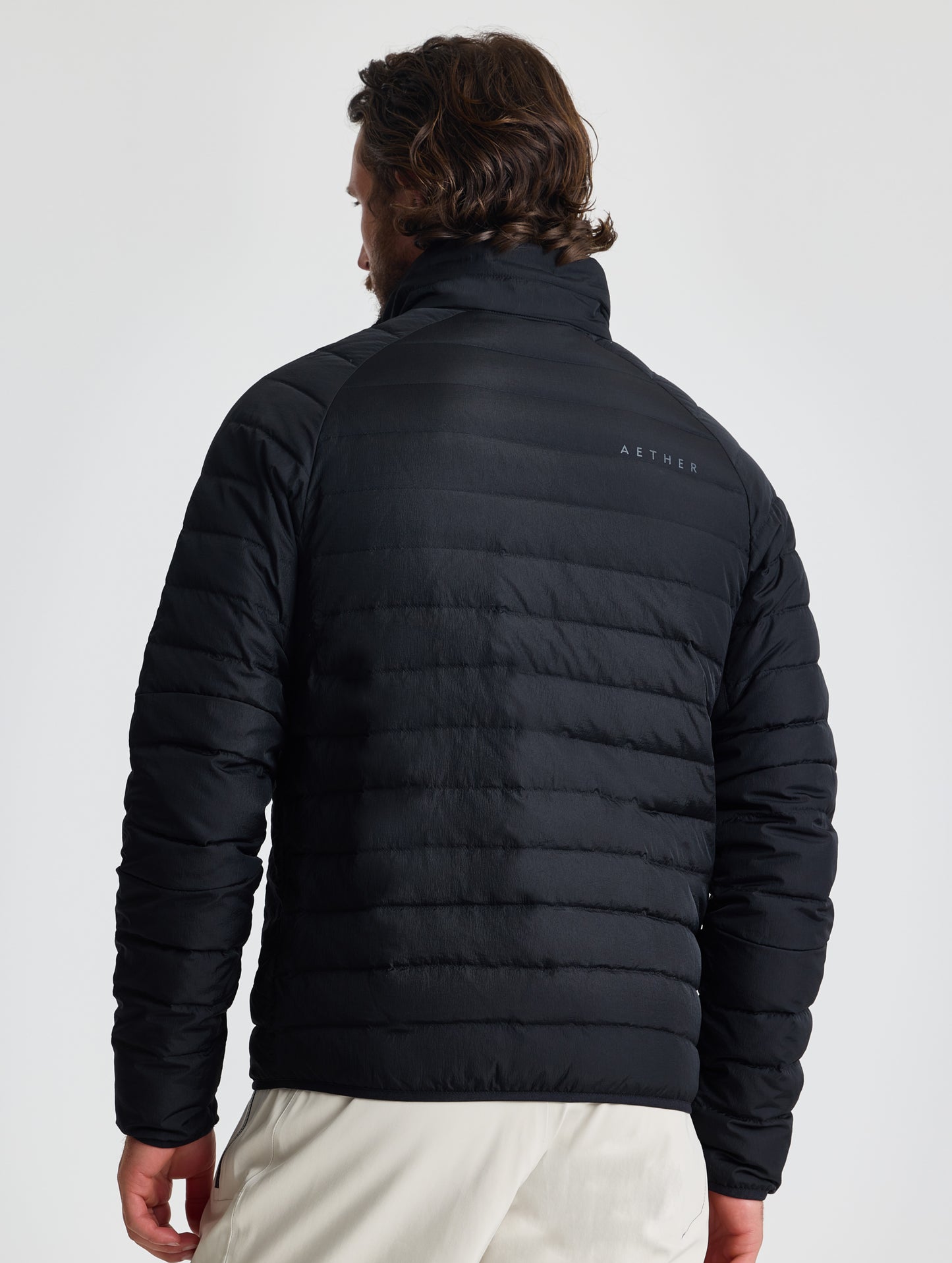 Rear view of man wearing Prospect Packable Down Jacket in Onyx Black from AETHER Apparel.