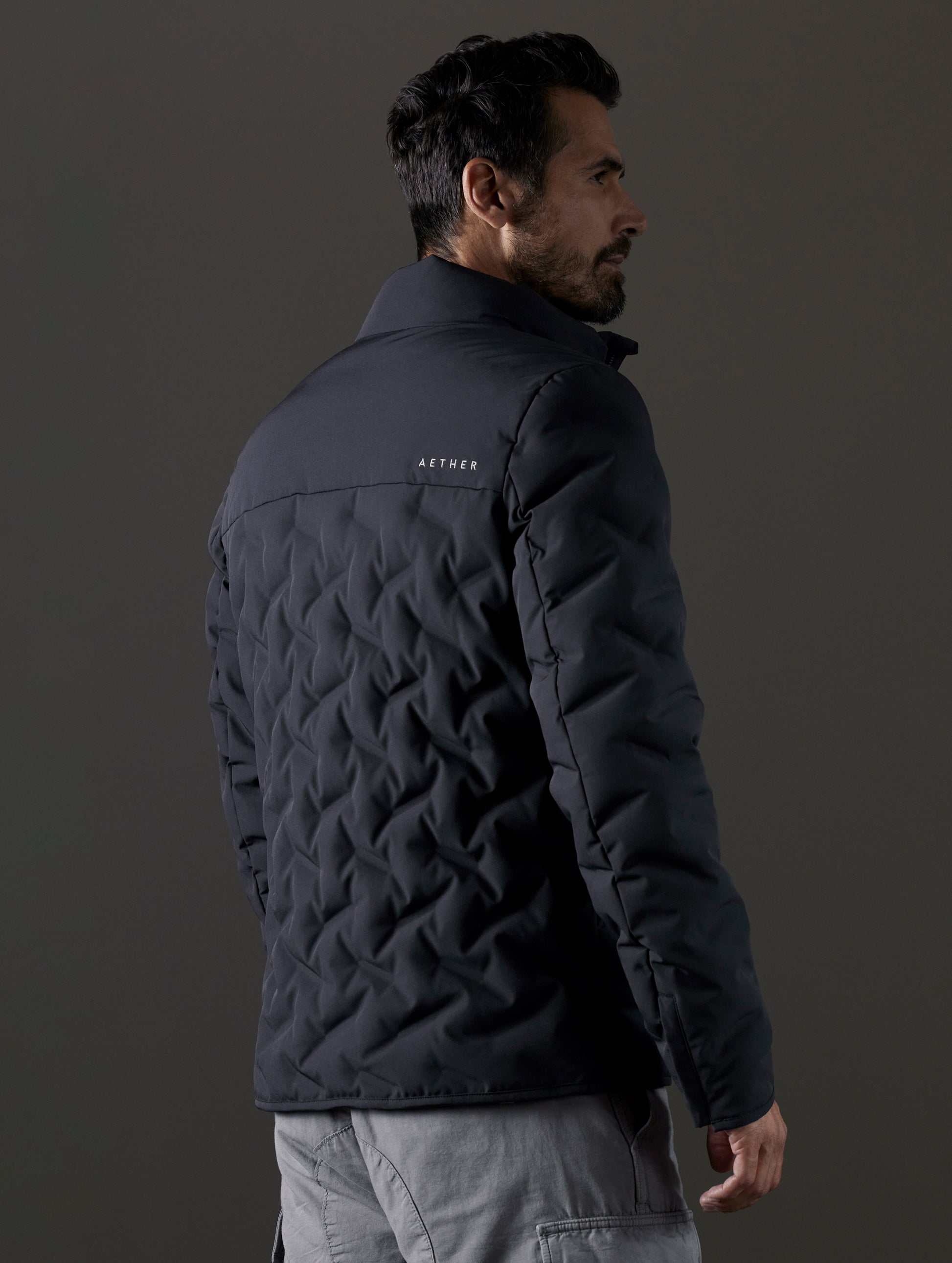 Rear 3/4 body view of man wearing Rex Down Jacket in Onyx Black  from AETHER Apparel.