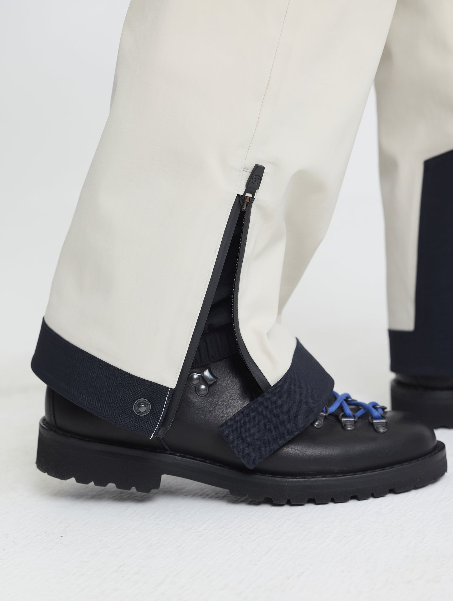 Closeup detailed view of the snap and zipper-secured adjustable leg cuff openings on the Ridge Insulated Snow Pant in Bone from AETHER Apparel.