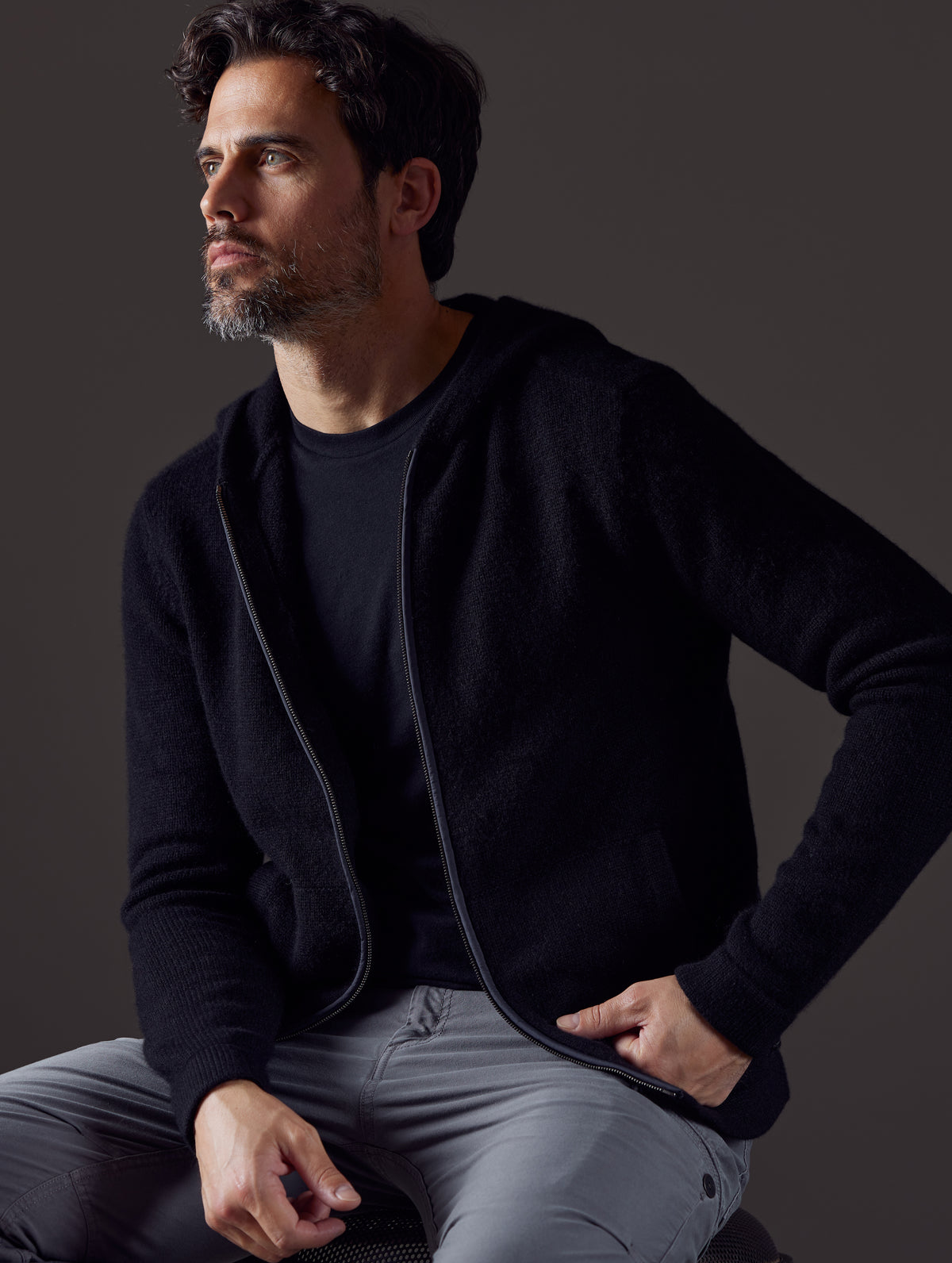 Front 3/4 body view of man sitting wearing Sawyer Cashmere Full-Zip in Onyx Black from AETHER Apparel.