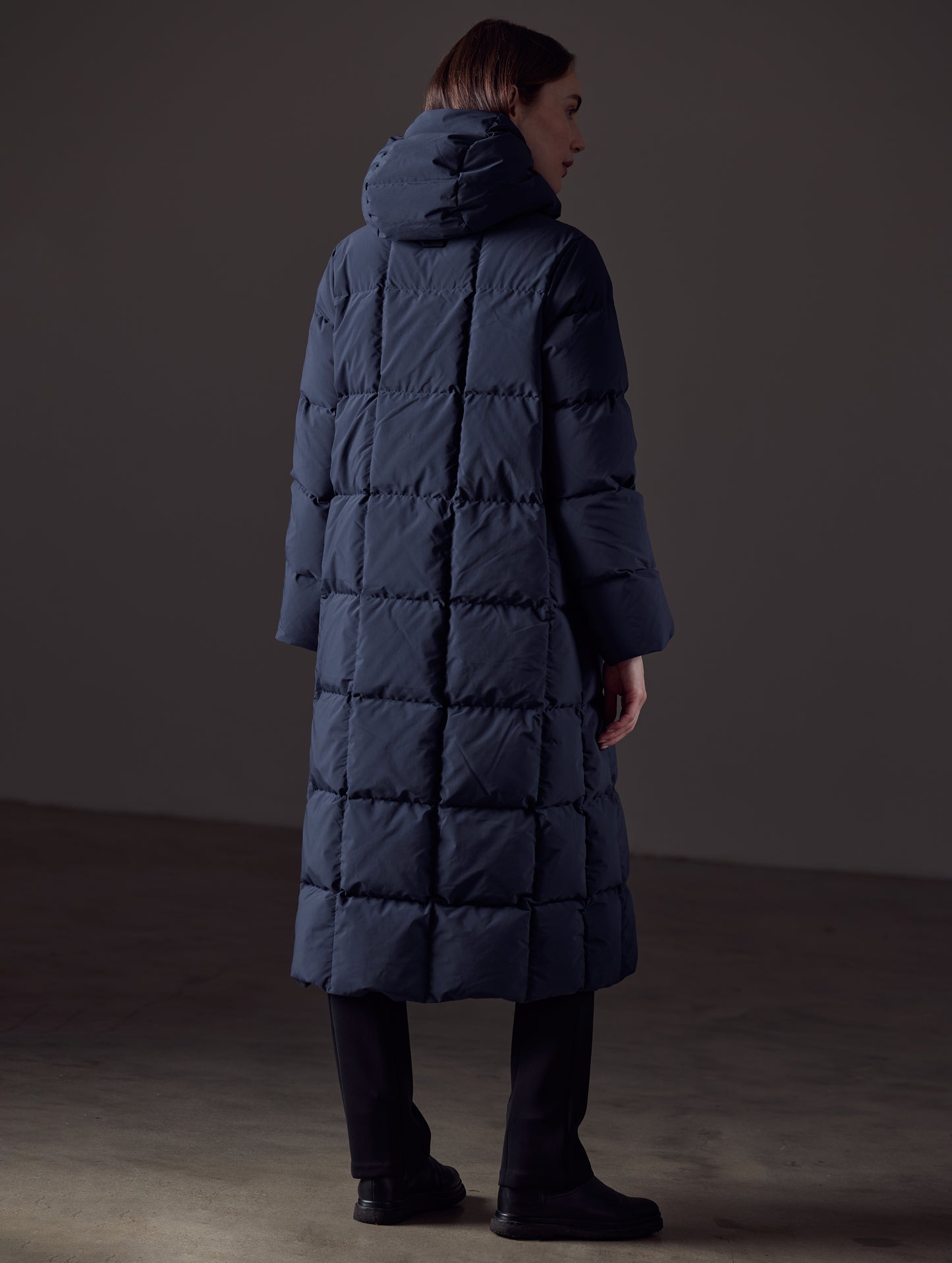 Rear angled full-body view of woman wearing Shaw Jacket in Nordic Navy Blue from AETHER Apparel.