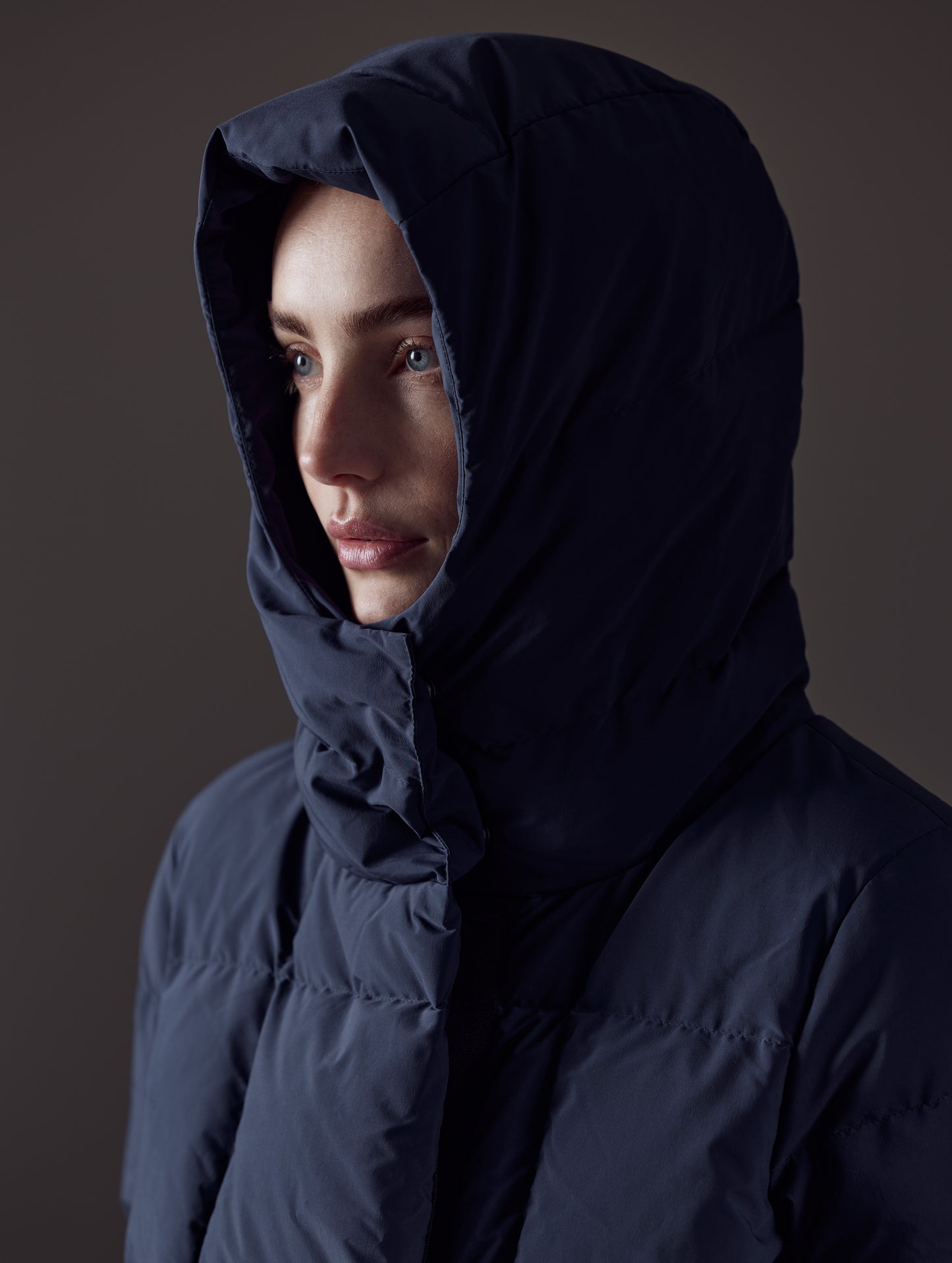 Closeup front angled view of woman with hood up wearing Shaw Jacket in Nordic Navy Blue from AETHER Apparel.