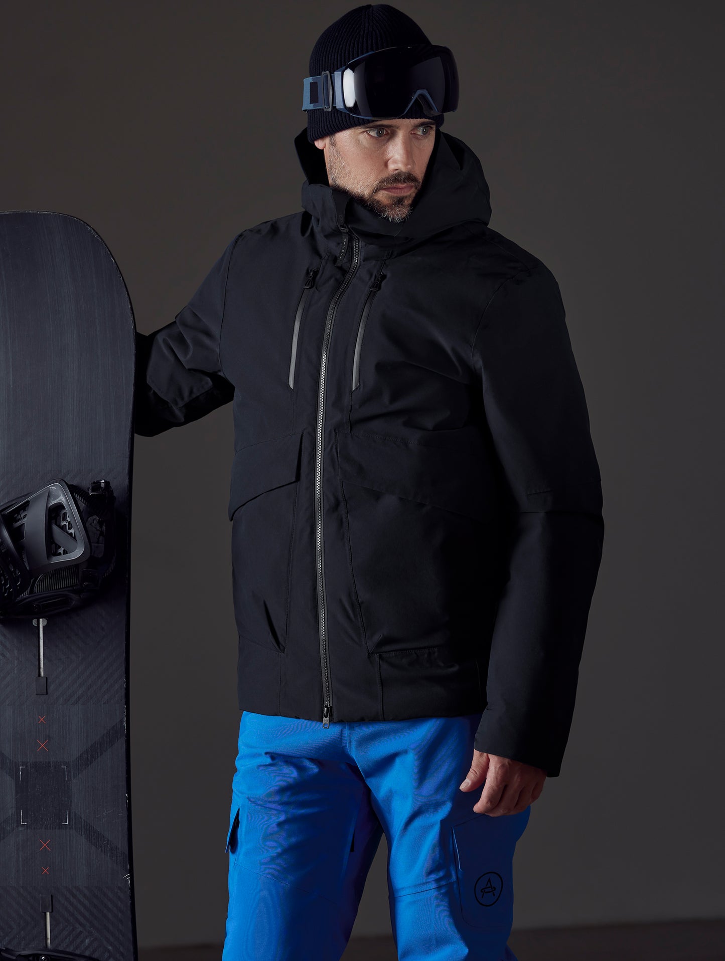 Front 3/4 body view of man holding snowboard wearing Silverton Down Jacket in Onyx Black from AETHER Apparel.