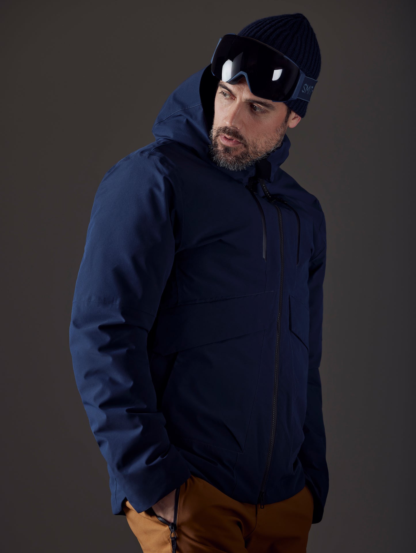 Front 3/4 body view of man with hand in pant pocket wearing Silverton Down Jacket in Total Eclipse dark blue from AETHER Apparel.