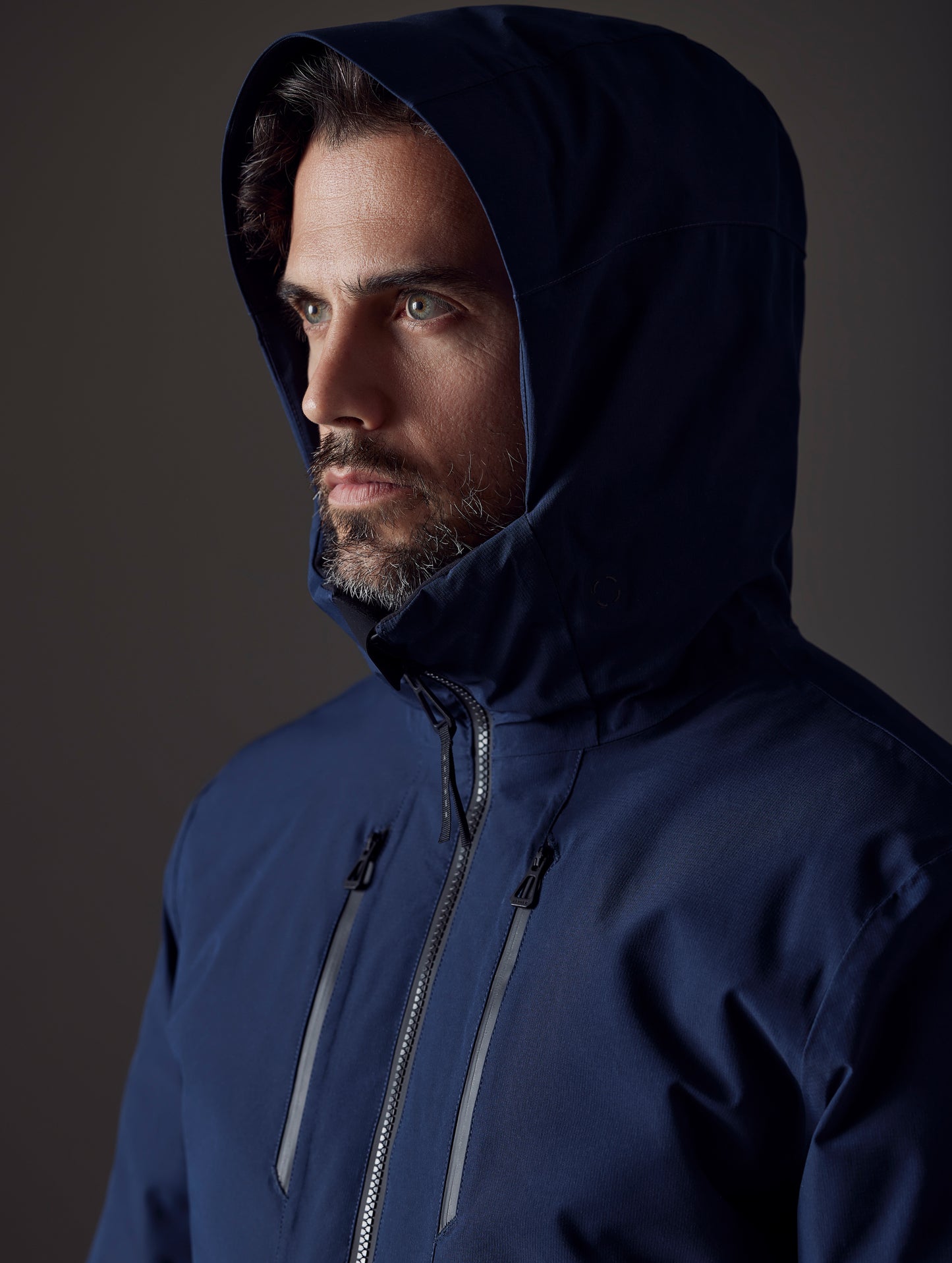 Closeup view of man with hood up wearing Silverton Down Jacket in Total Eclipse dark blue from AETHER Apparel.