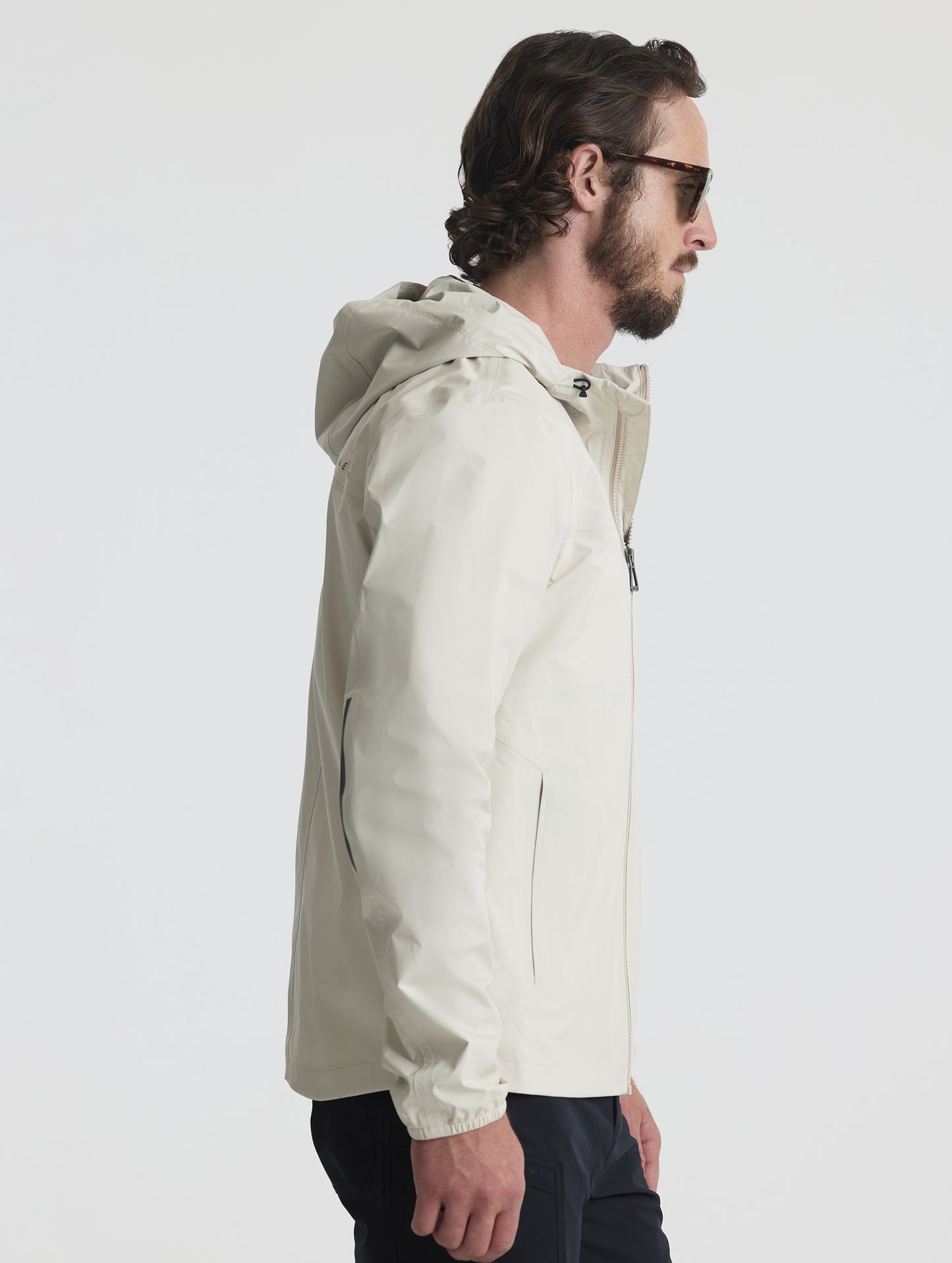Right profile view of man wearing Storm All-Weather Jacket in Bone white from AETHER Apparel.