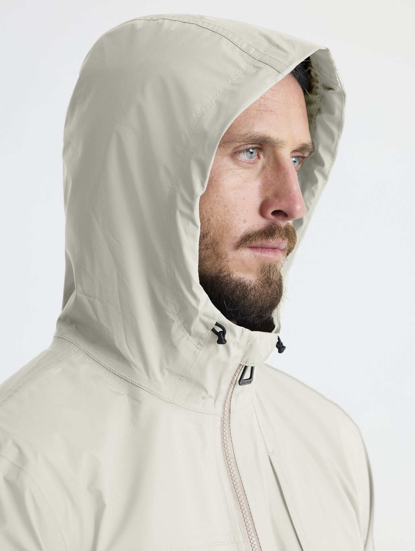 Man wearing hood of Storm All-Weather Jacket in Bone white from AETHER Apparel.