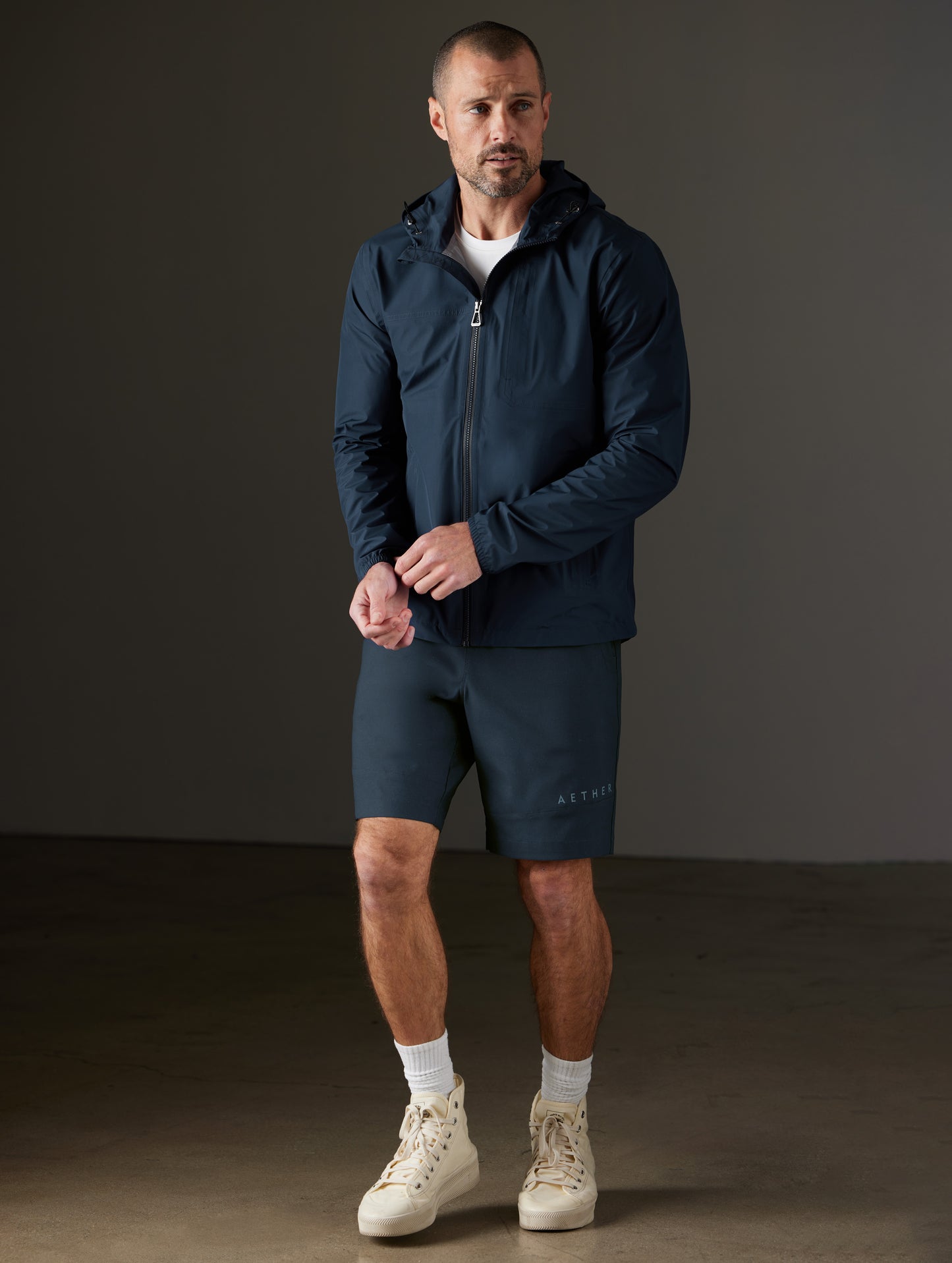 Front 3/4 full-body view of man wearing Storm All-Weather Jacket in Total Eclipse dark blue from AETHER Apparel.