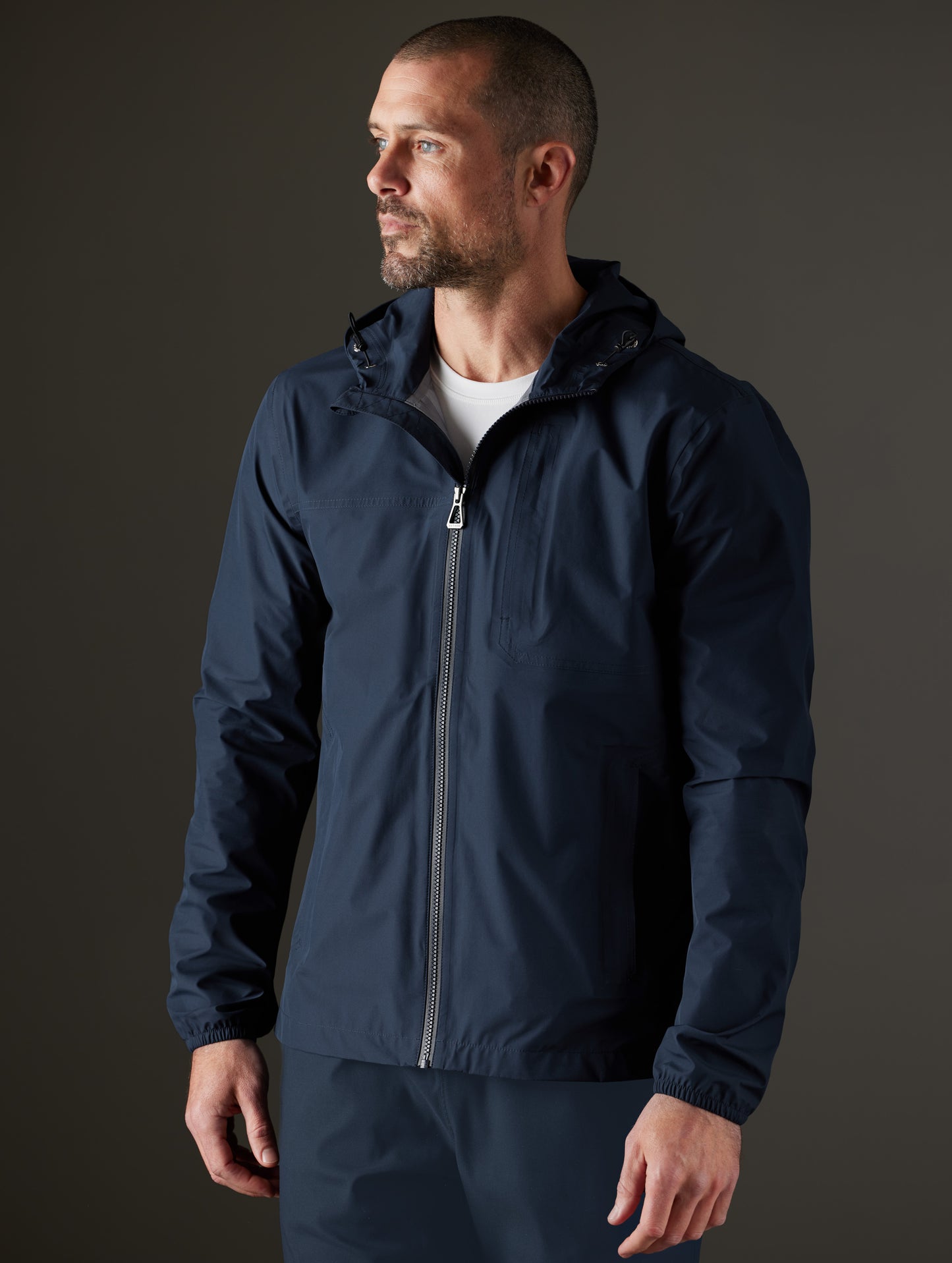 Front 3/4 body view of man wearing Storm All-Weather Jacket in Total Eclipse dark blue from AETHER Apparel.