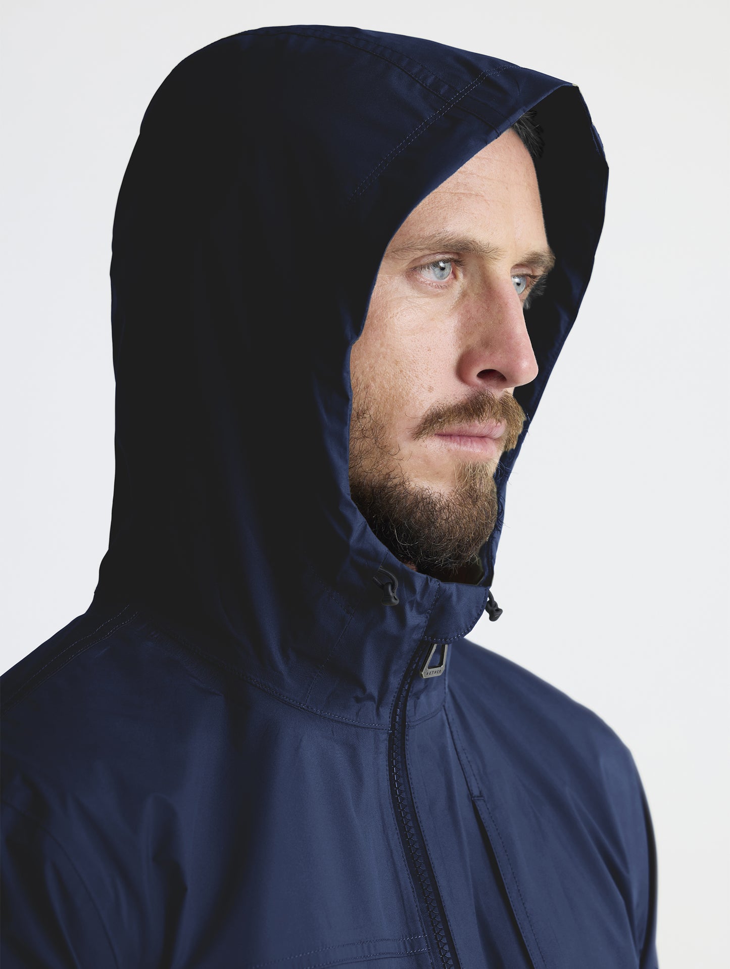 Man wearing hood of Storm All-Weather Jacket in Total Eclipse dark blue from AETHER Apparel.