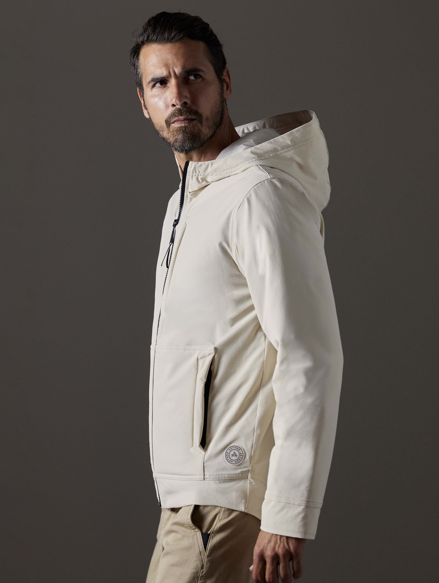 Side profile body view of man wearing Stornaway Insulated Hoodie in Bone white from AETHER Apparel.