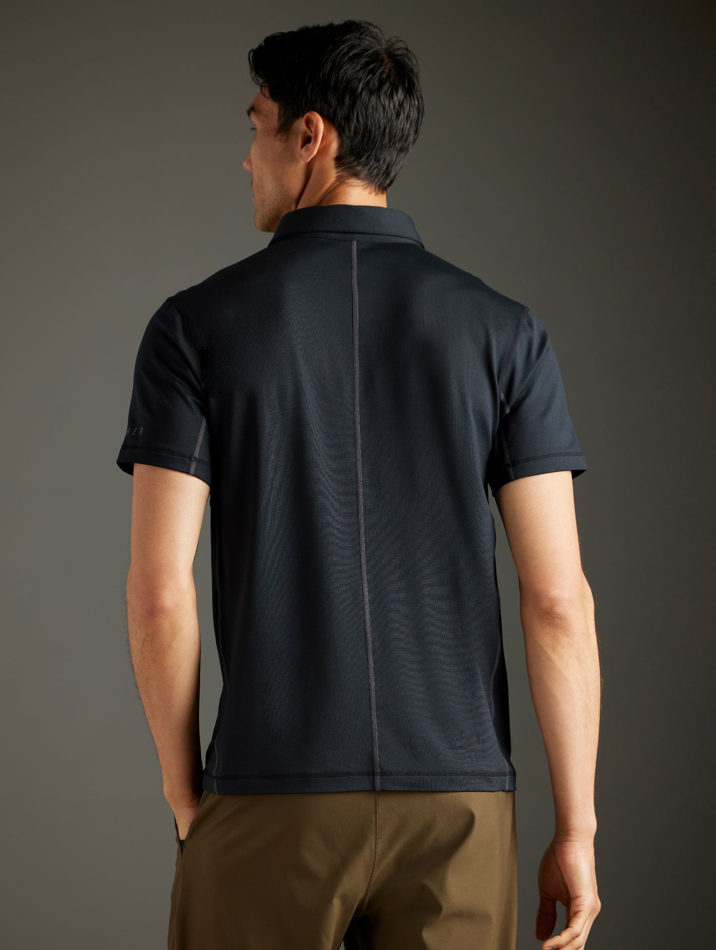 Rear body view of man wearing Trek Articulated Polo in Onyx Black from AETHER Apparel.